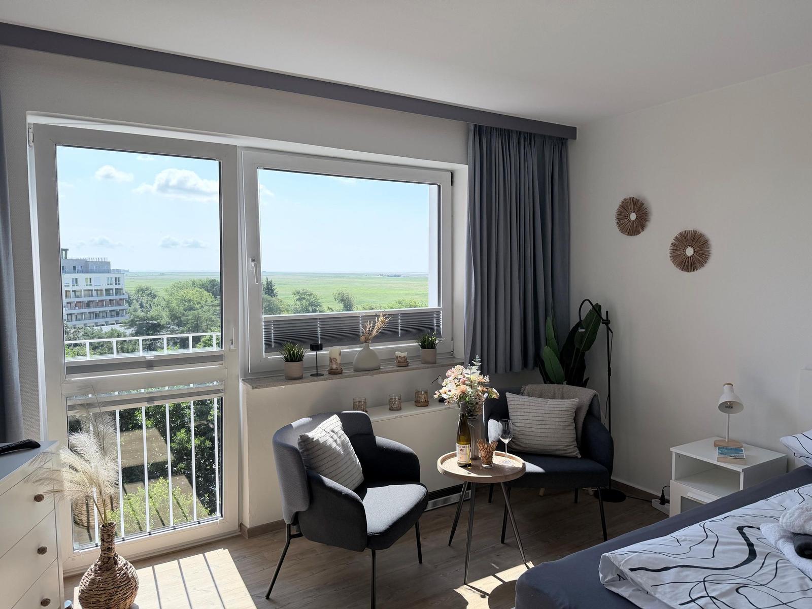 Zimmer mit Blick auf Grünfläche und Balkon. Möbel, Pflanzen und Wanddekoration.