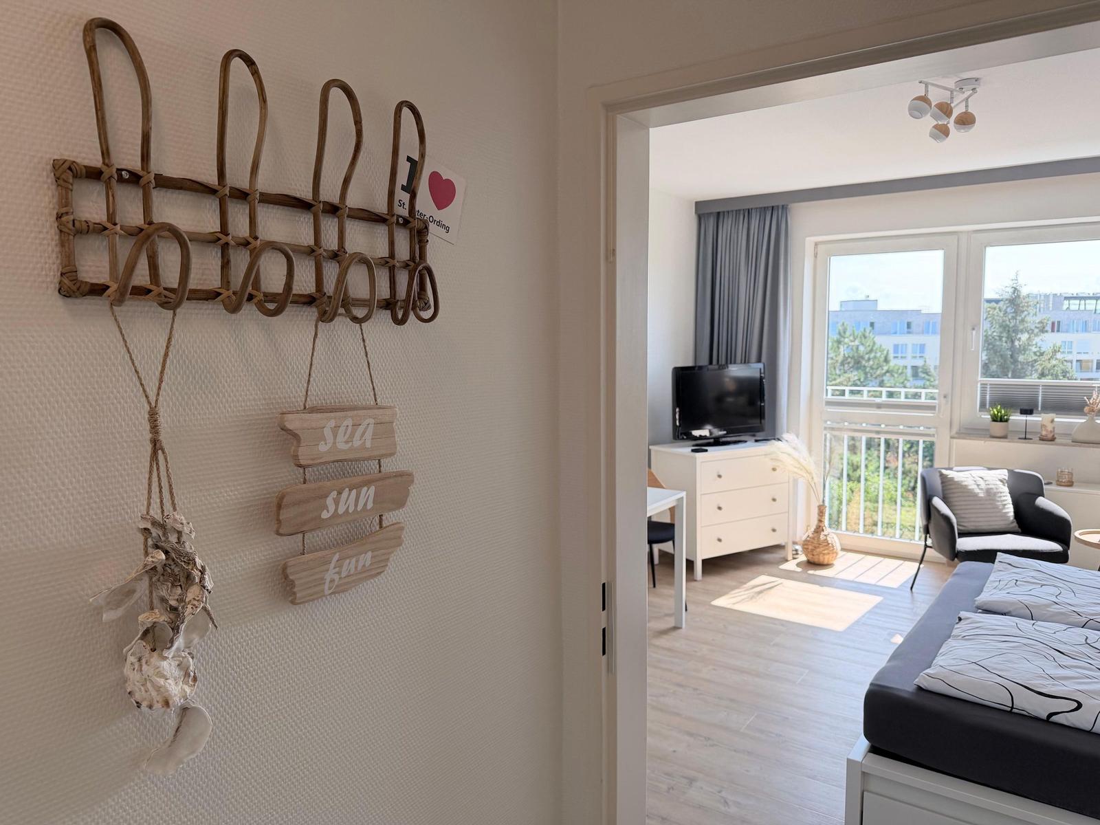 Wohnung mit Blick auf Balkon, Bett und TV. Wanddekoration mit Meeresmotiven.