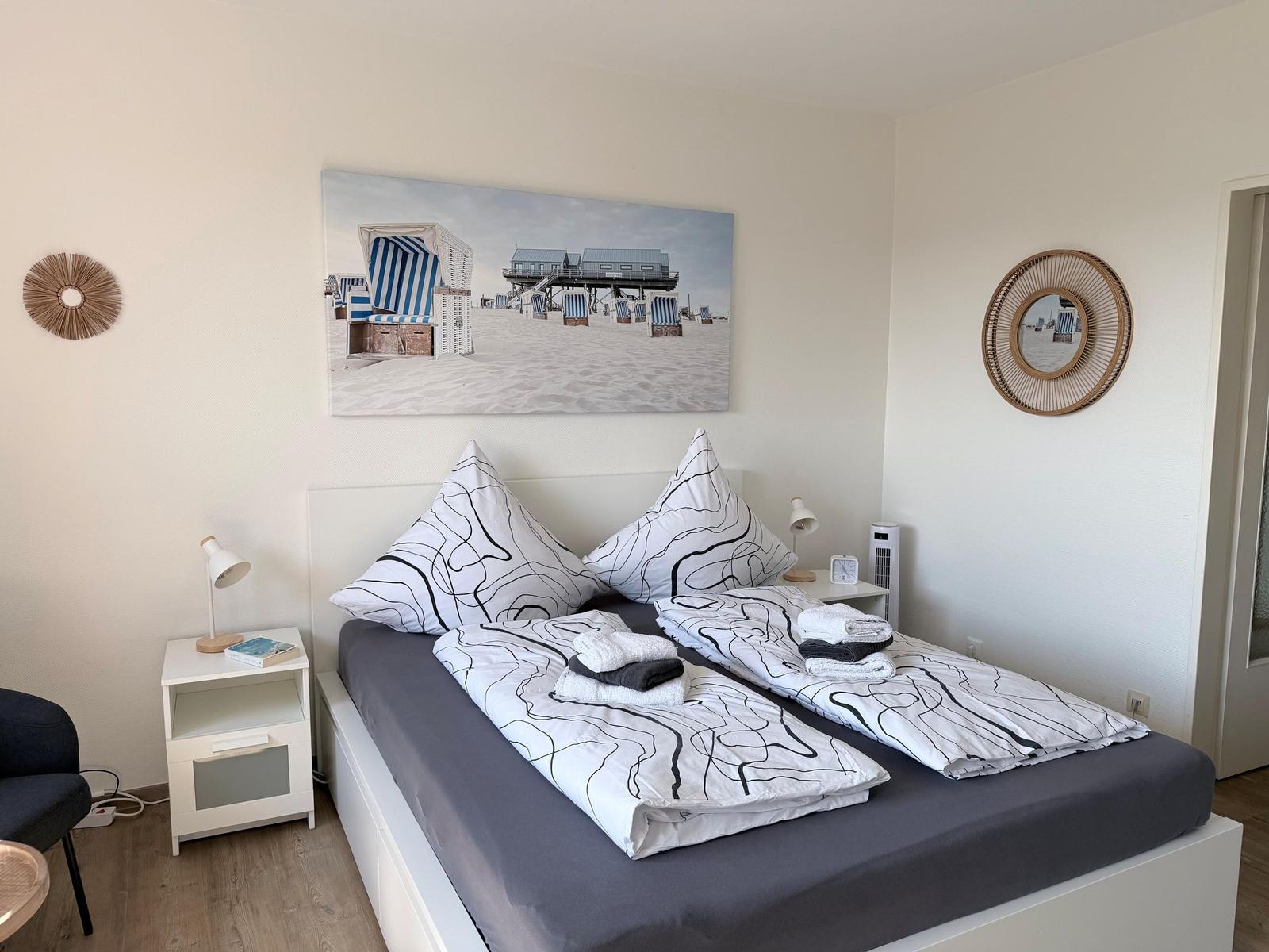 Schlafzimmer mit Bett, Nachttischen und Wandbild. Decke und Kissen mit schwarz-weißem Muster.