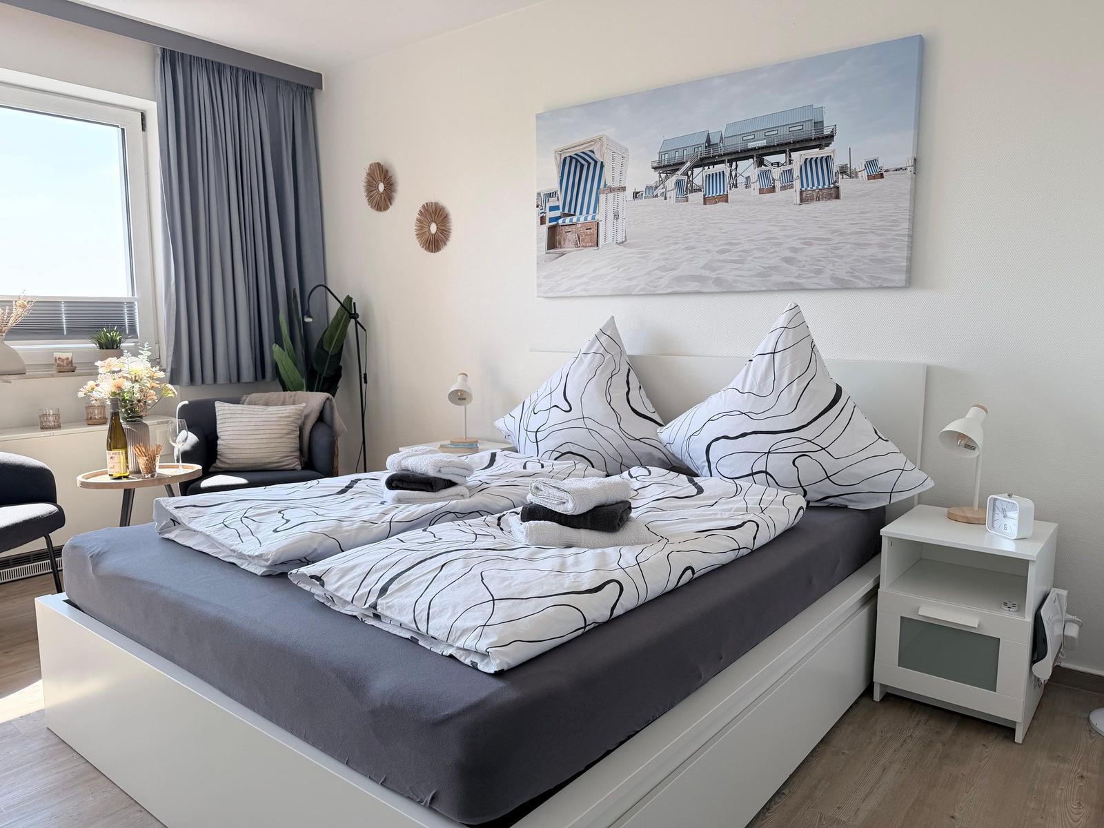 Schlafzimmer mit Doppelbett, Wandbild Strand, Nachttisch und Fenster.