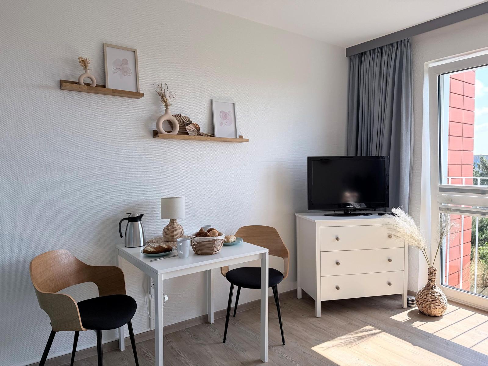 Wohnzimmer mit Esstisch, Fernseher und Fensterblick.