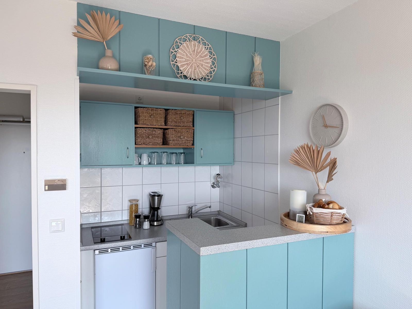 Küche mit hellblauen Schränken, Arbeitsplatte und Spüle. Dekoration mit Trockenpflanzen und Korb.