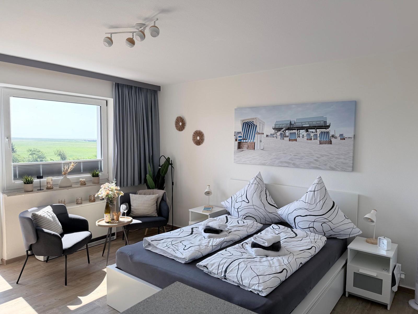 Schlafzimmer mit Doppelbett, Sitzgelegenheit und Blick auf Felder.