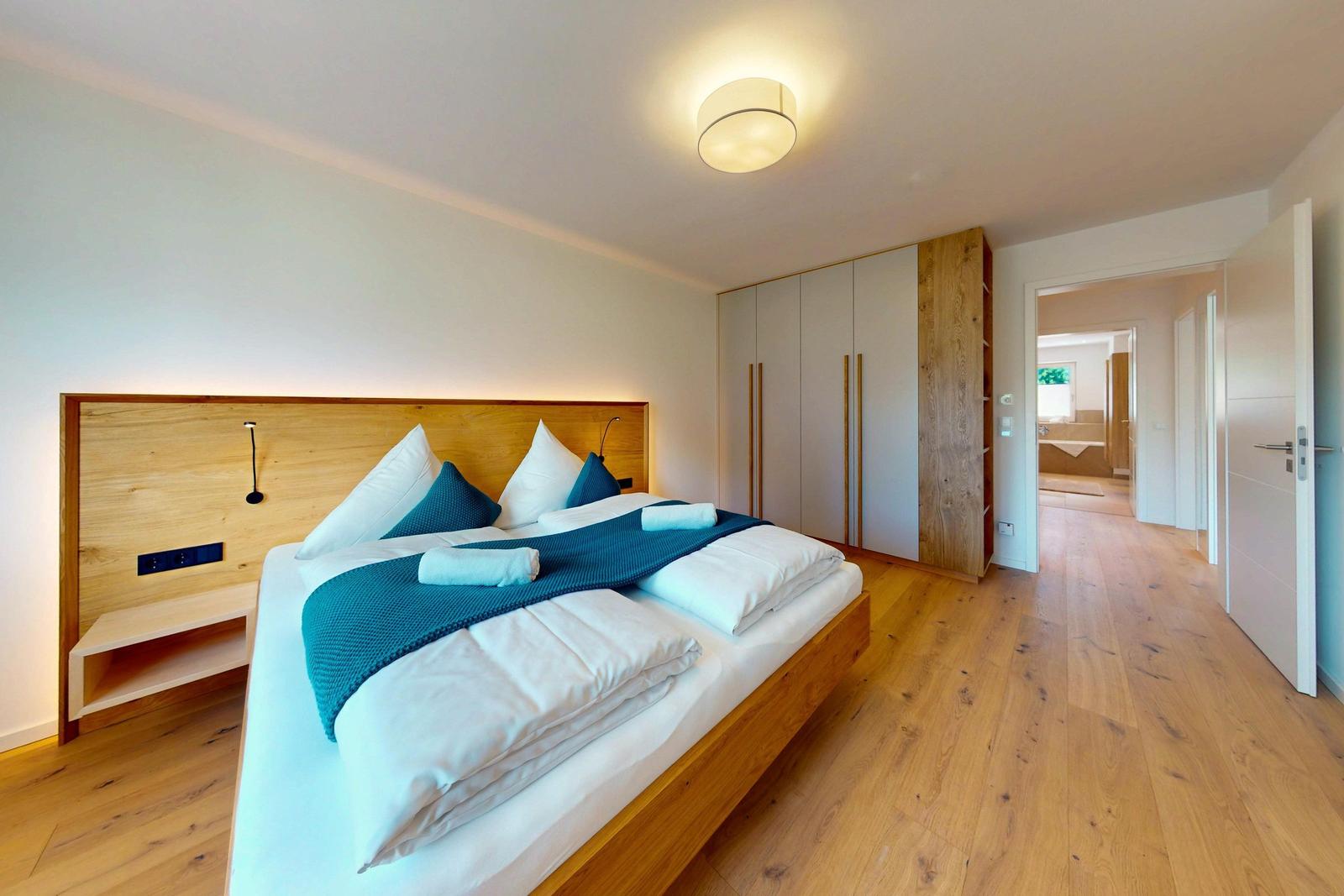 Schlafzimmer mit Holzbett, Kleiderschrank und Blick in die Badewanne.