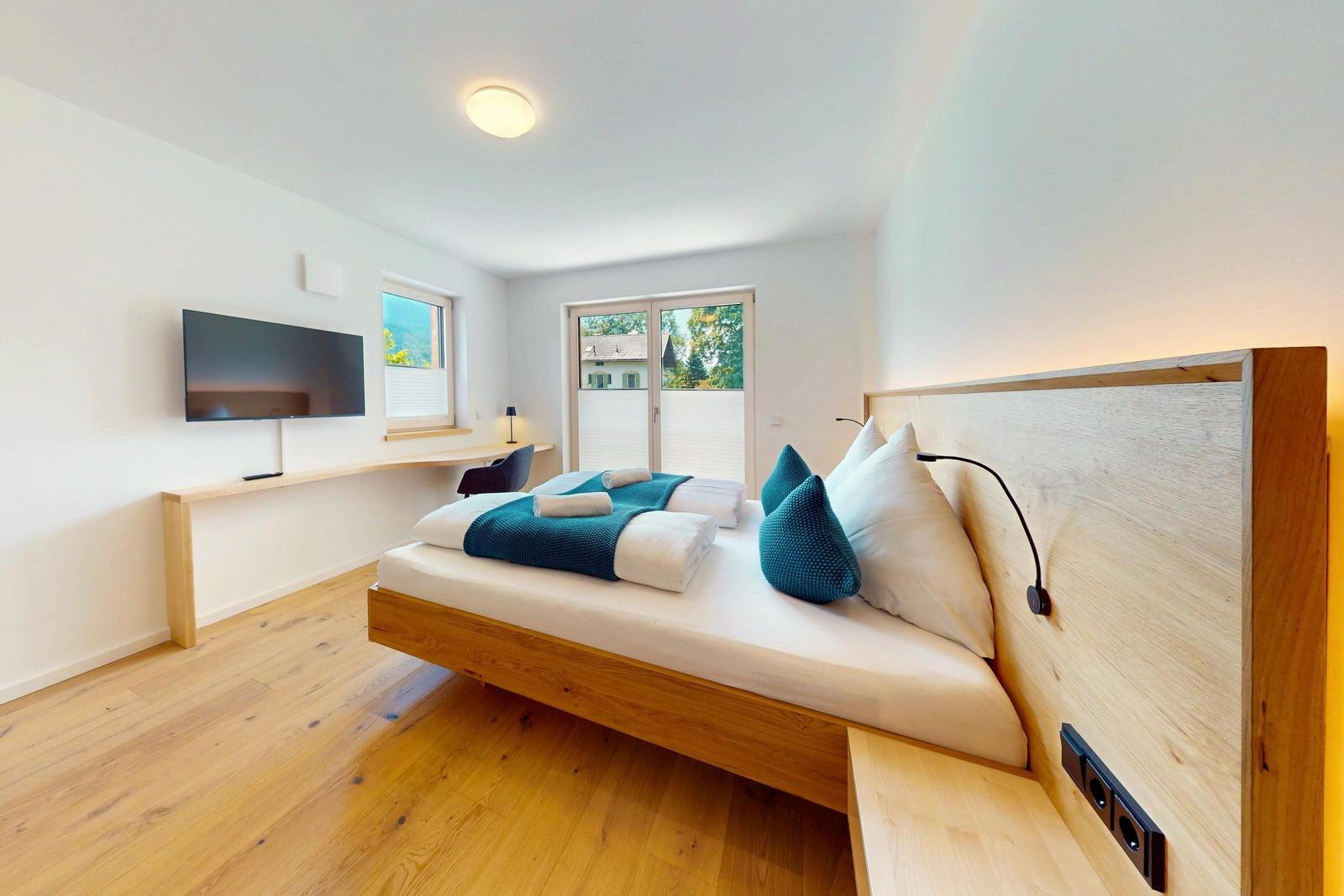 Schlafzimmer mit Bett, TV und Fenster. Holzboden und Wandgestaltung.