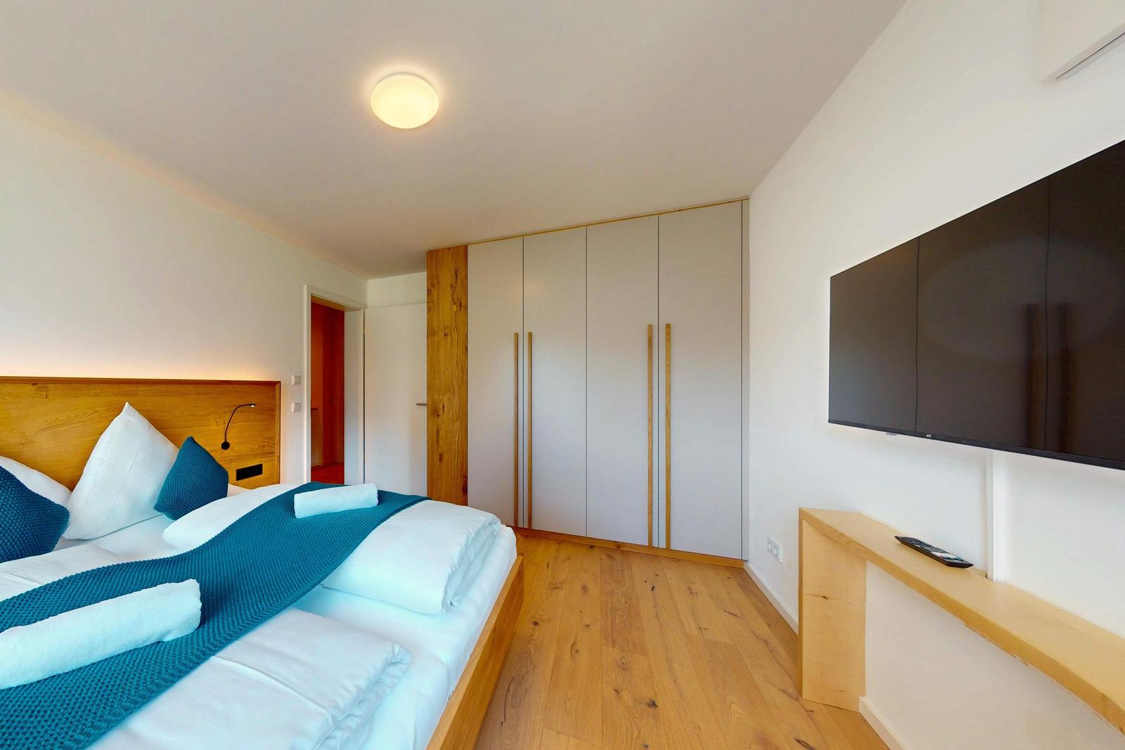 Schlafzimmer mit Bett, Kleiderschrank und Wand-TV.