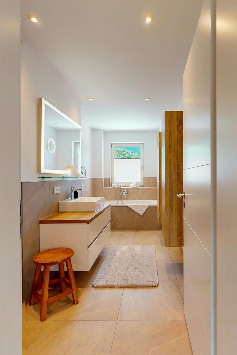 Badezimmer mit Badewanne, Waschbecken und Spiegel. Holzakzent und Teppich.