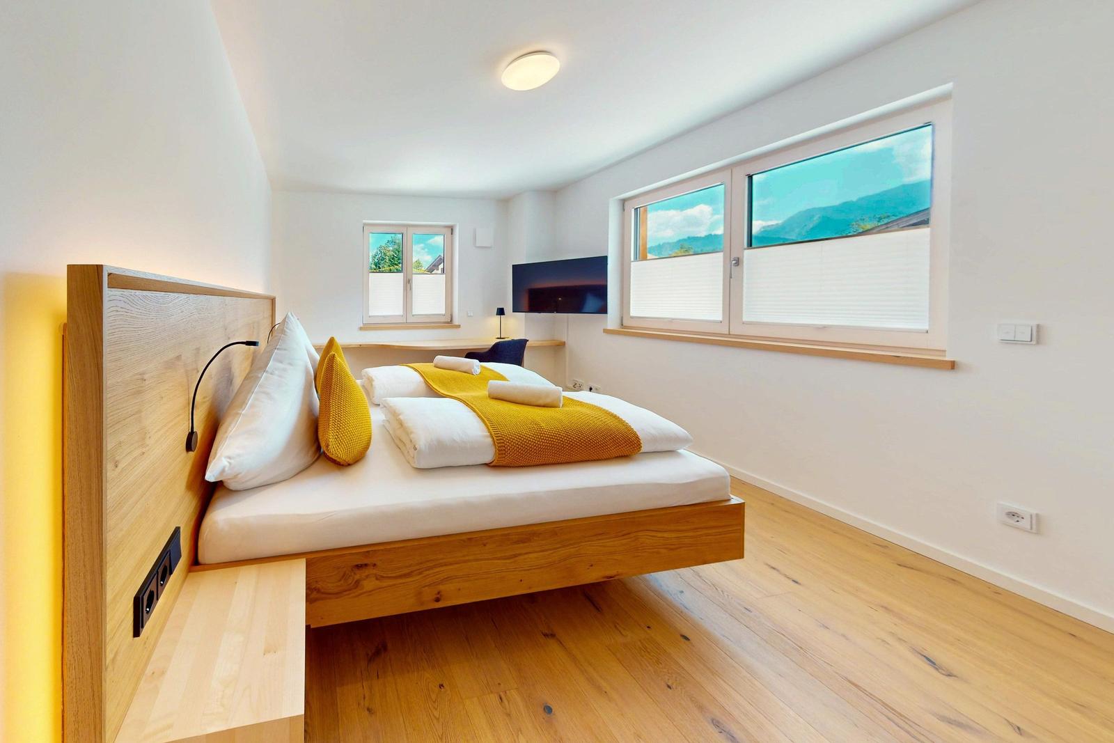 Schlafzimmer mit Holzbett, Fenstern und Fernseher