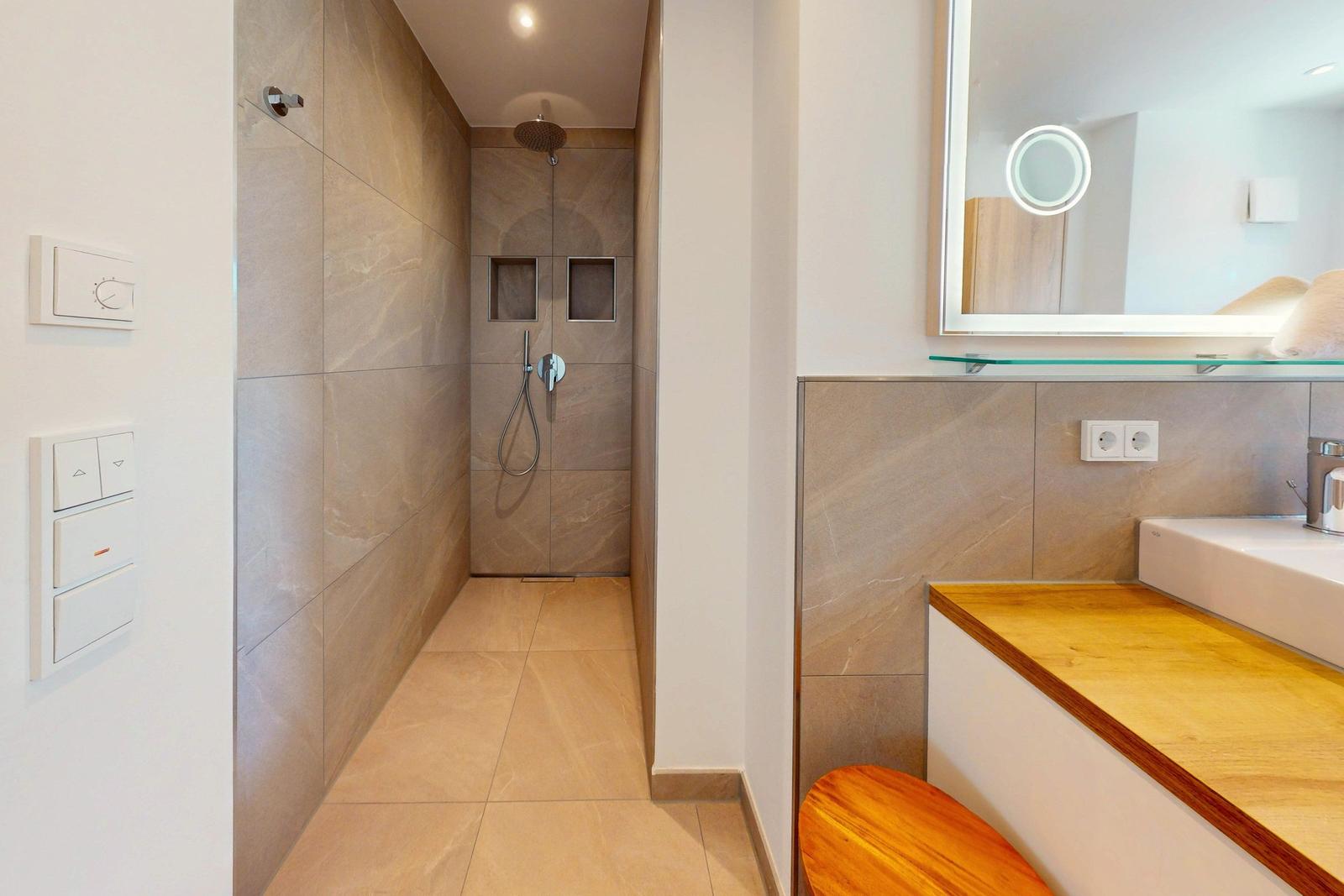 Dusche mit Duschbrause und Handbrause, Waschbecken mit Spiegel und Holzoberfläche.
