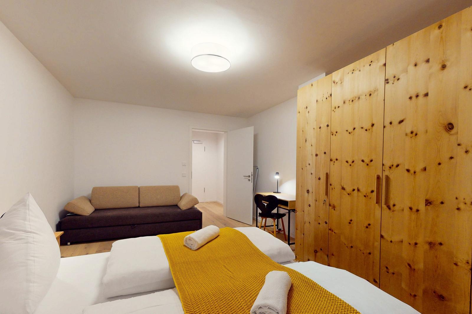 Schlafzimmer mit Bett, Sofa, Schreibtisch und Holzschrank.
