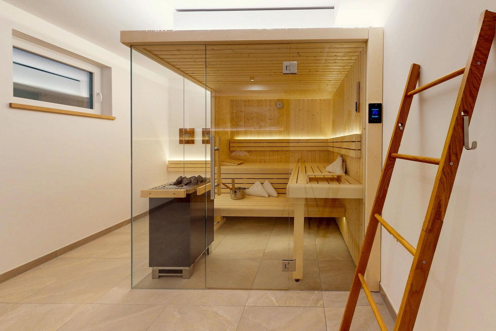 Sauna mit Holzbank, Glaswand und digitaler Steuerung. Holzstufen und Fenster sichtbar.
