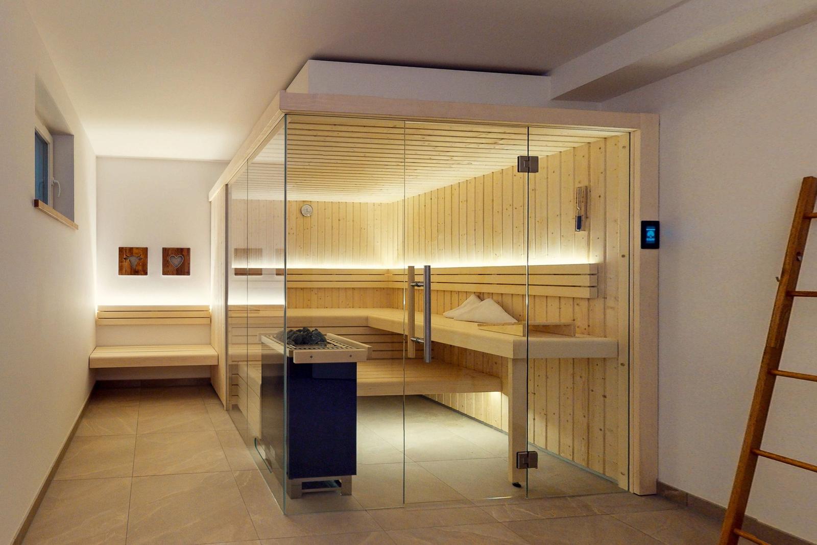 Sauna mit Glasfront und Holzbank. Nebenraum mit Sitzbank und Wandbildern.