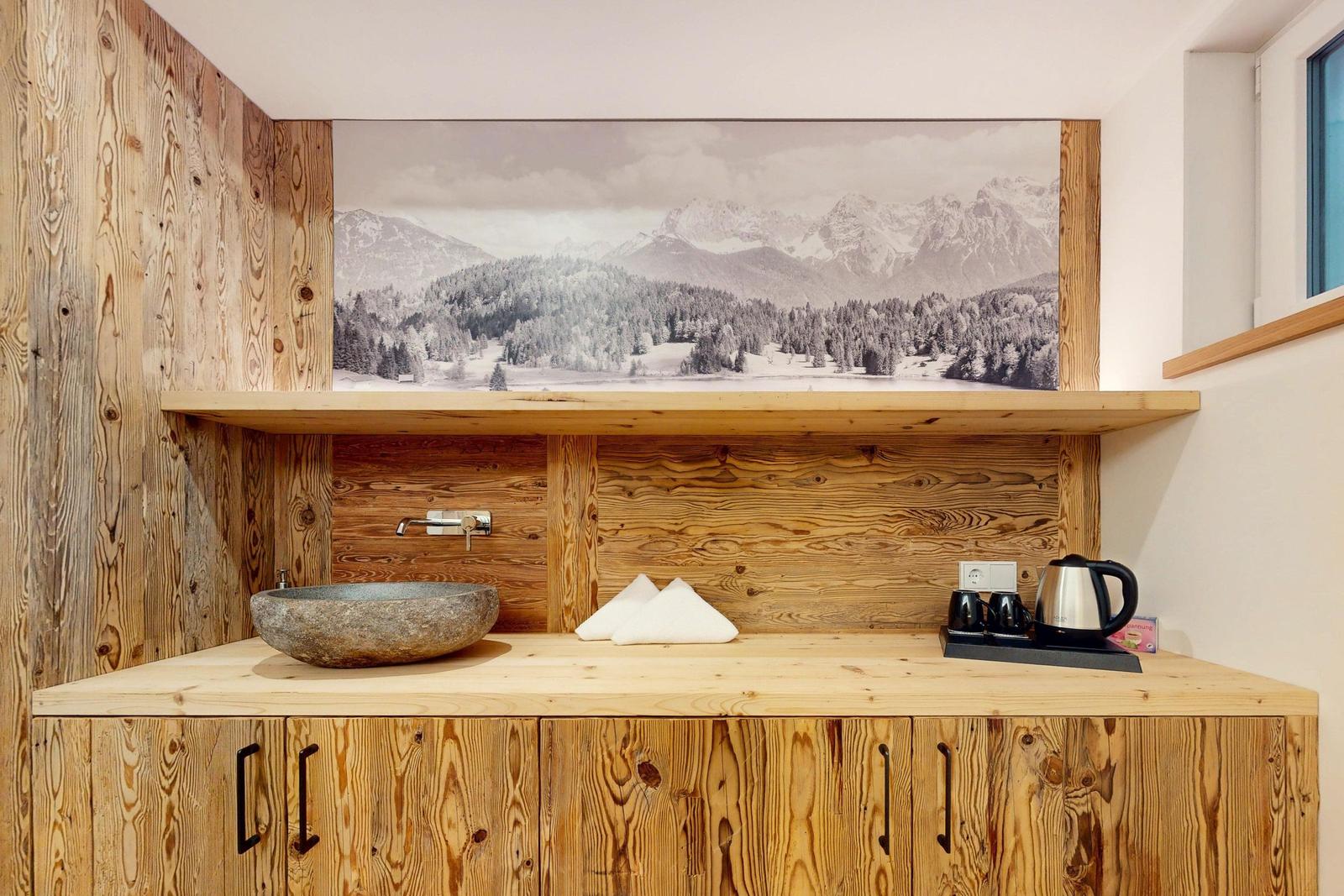 Holzvertäfelte Wand mit Waschbecken und Bergbild. Kaffeebereiter und Handtücher auf Arbeitsfläche.