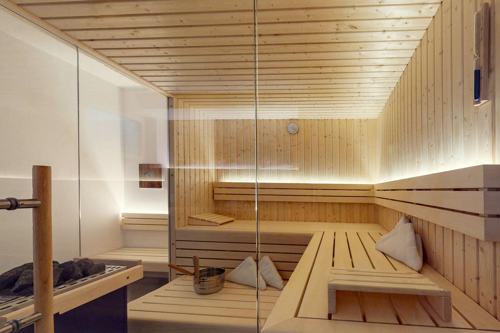 Sauna mit Holzbank, Steine und Kissen. Glaswand und Holzwände.