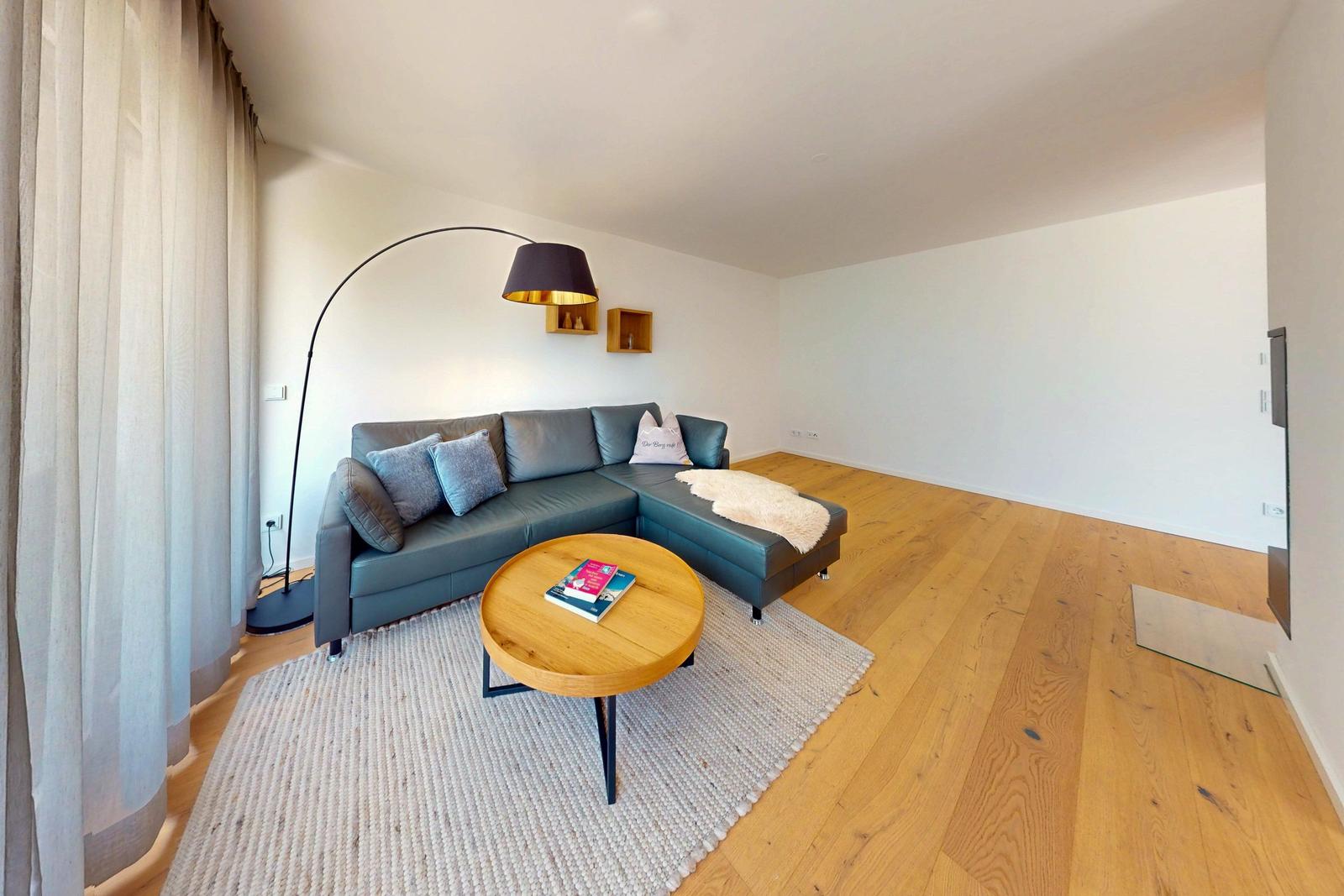 Wohnzimmer mit grauem Sofa, runden Tisch und Holzboden.