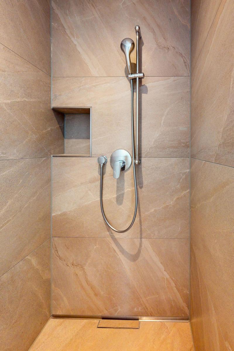 Dusche mit Handbrause und Wandhalterung, befestigt an marbled Wänden.