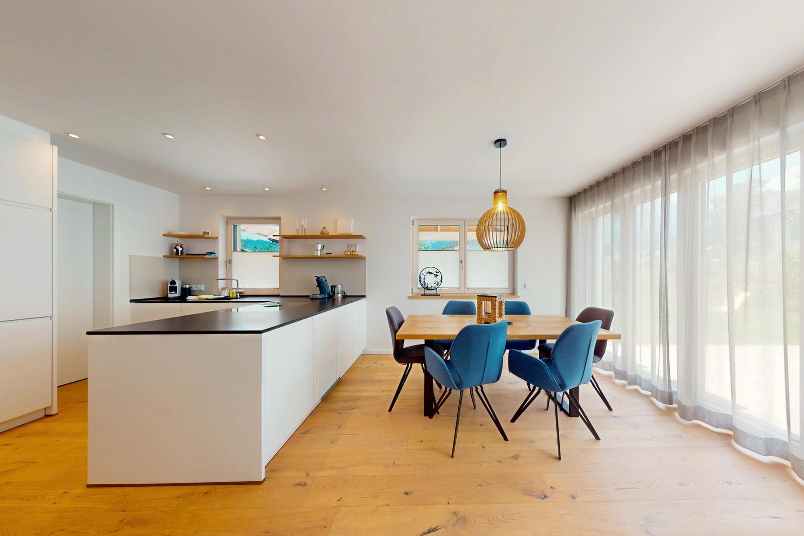 Moderne Küche mit Essbereich und großem Fenster. Holzboden und blaue Stühle.