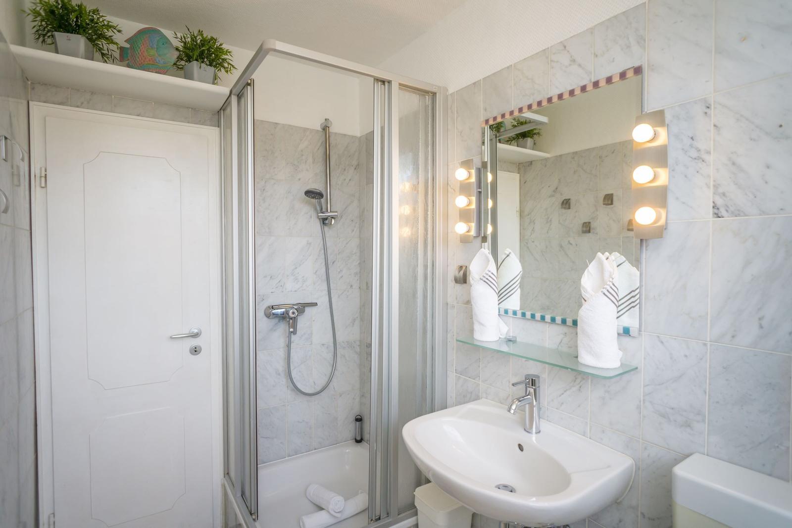 Badezimmer mit Dusche, Waschbecken und Spiegel mit Licht