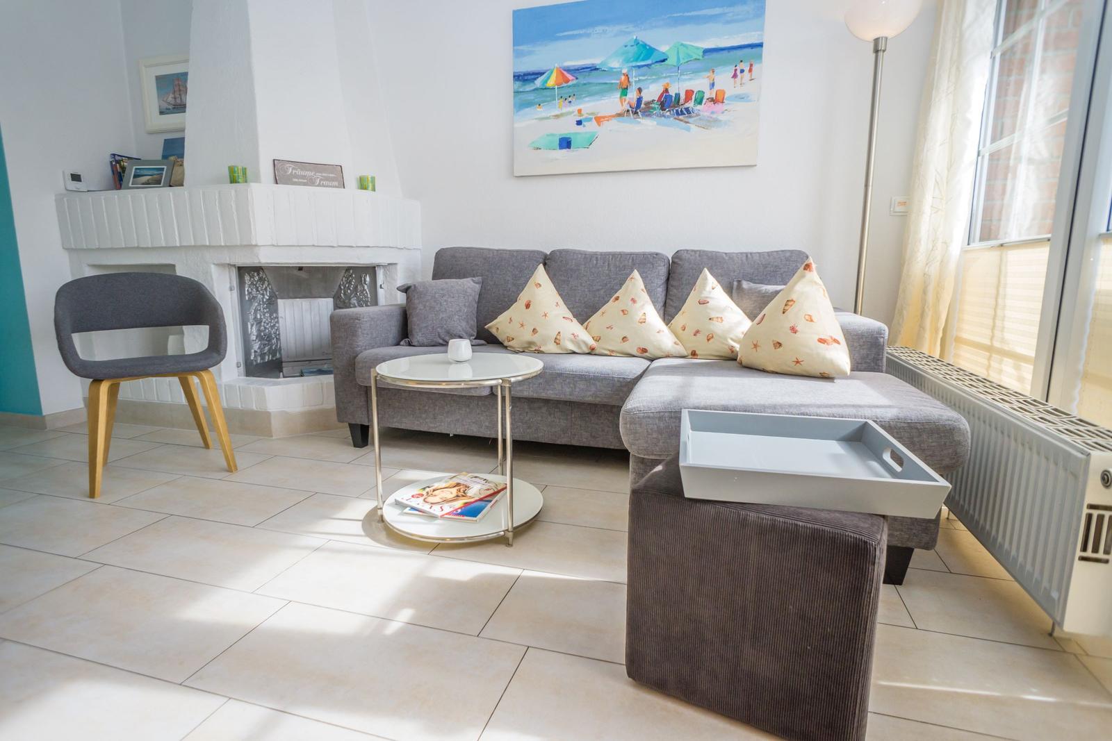 Wohnzimmer mit grauem Sofa, Kamin und Strandbild an der Wand.