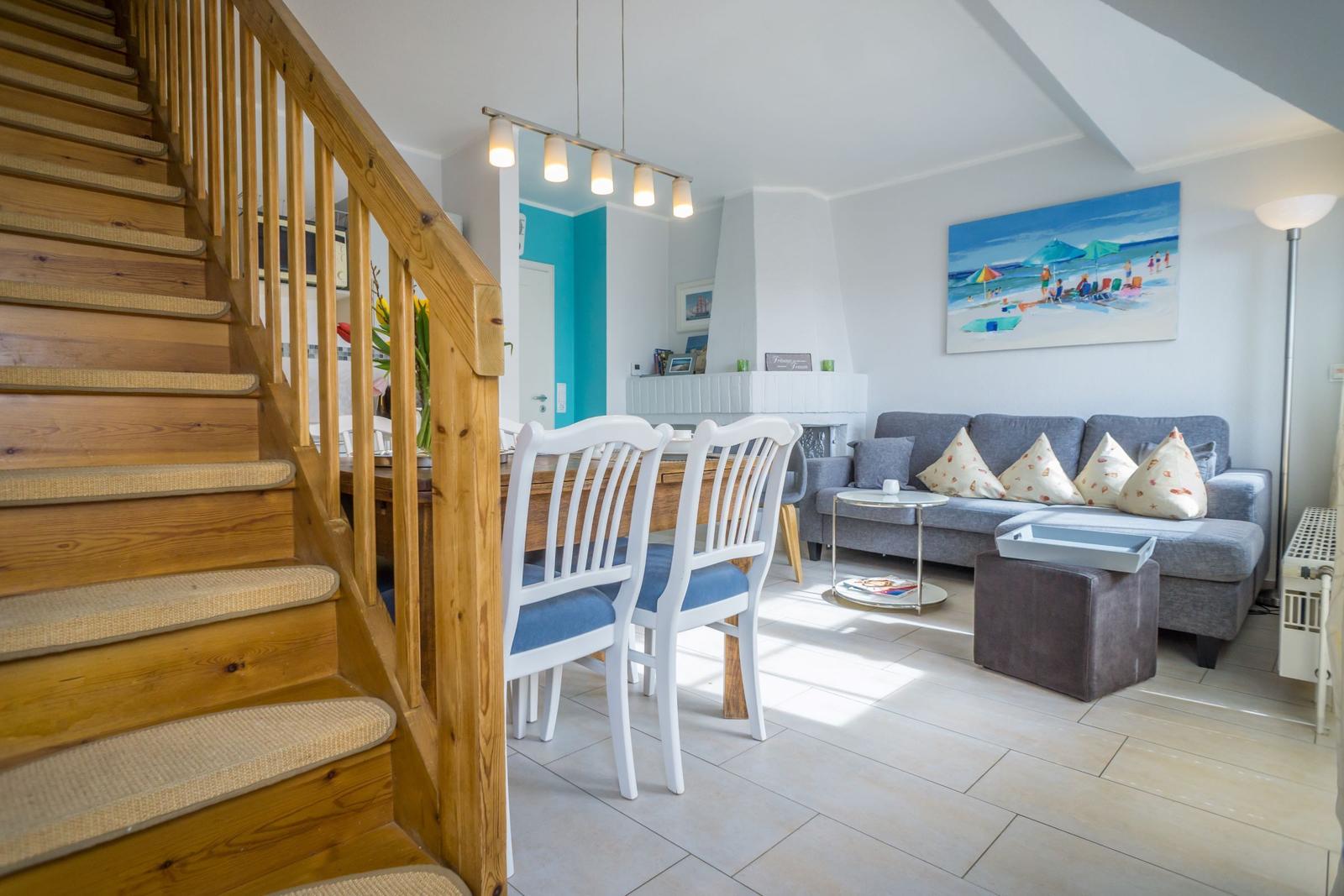 Wohn- und Essbereich mit Holztreppe, Sofa und Küchenbereich im Hintergrund.