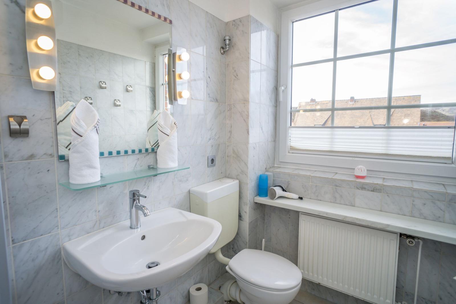 Badezimmer mit Waschbecken, Toilette und Fenster mit Blick auf Dächer.