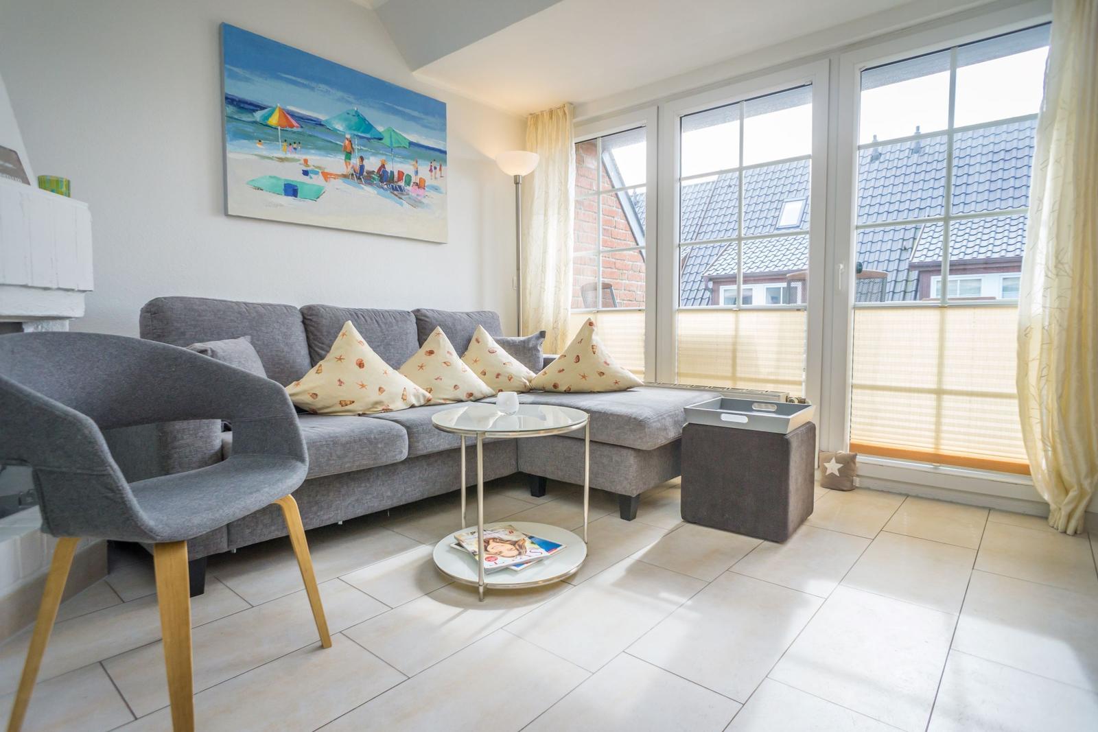 Wohnzimmer mit grauem Sofa, Tisch und großen Fenstern.