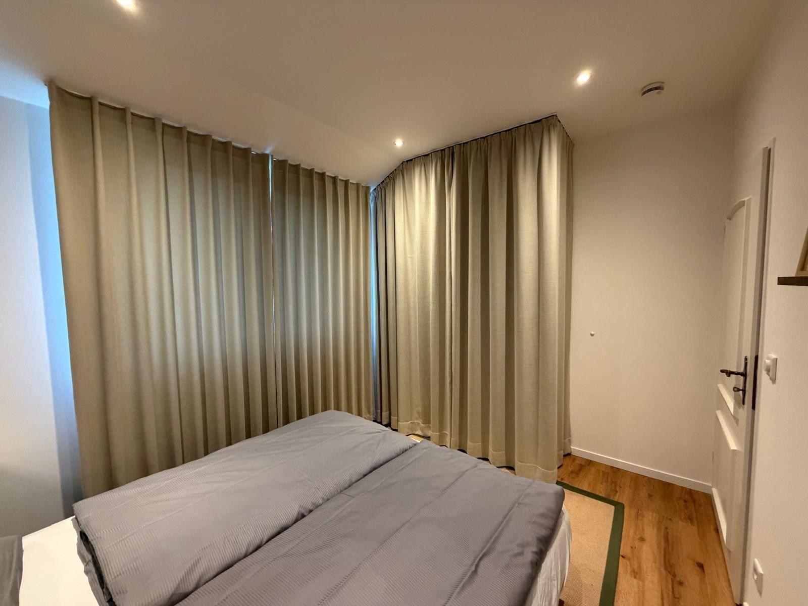 Schlafzimmer mit Bett, Holzboden und schweren Vorhängen.