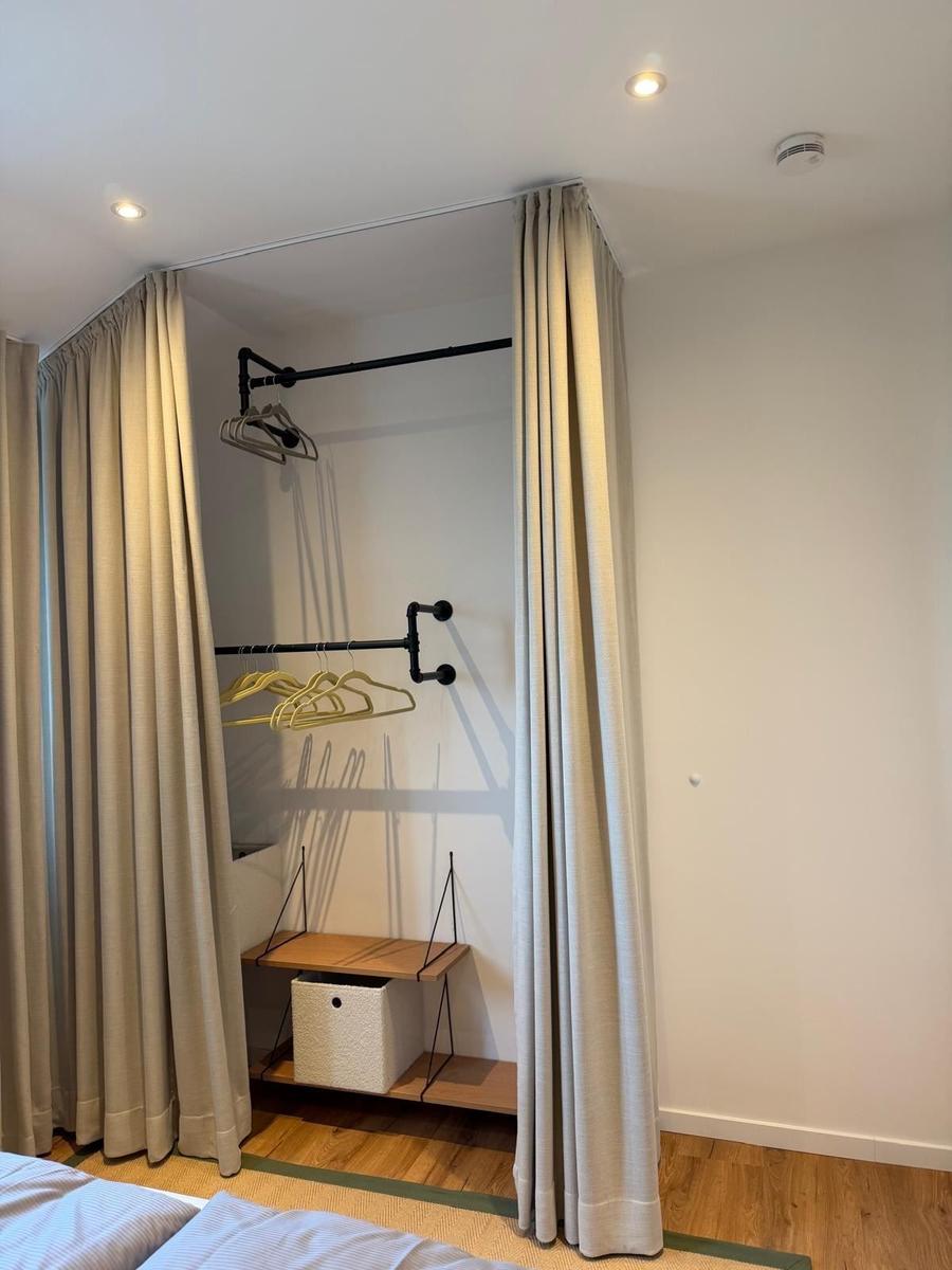 Schlafzimmer mit Kleiderschrank, Vorhängen und Holzboden.