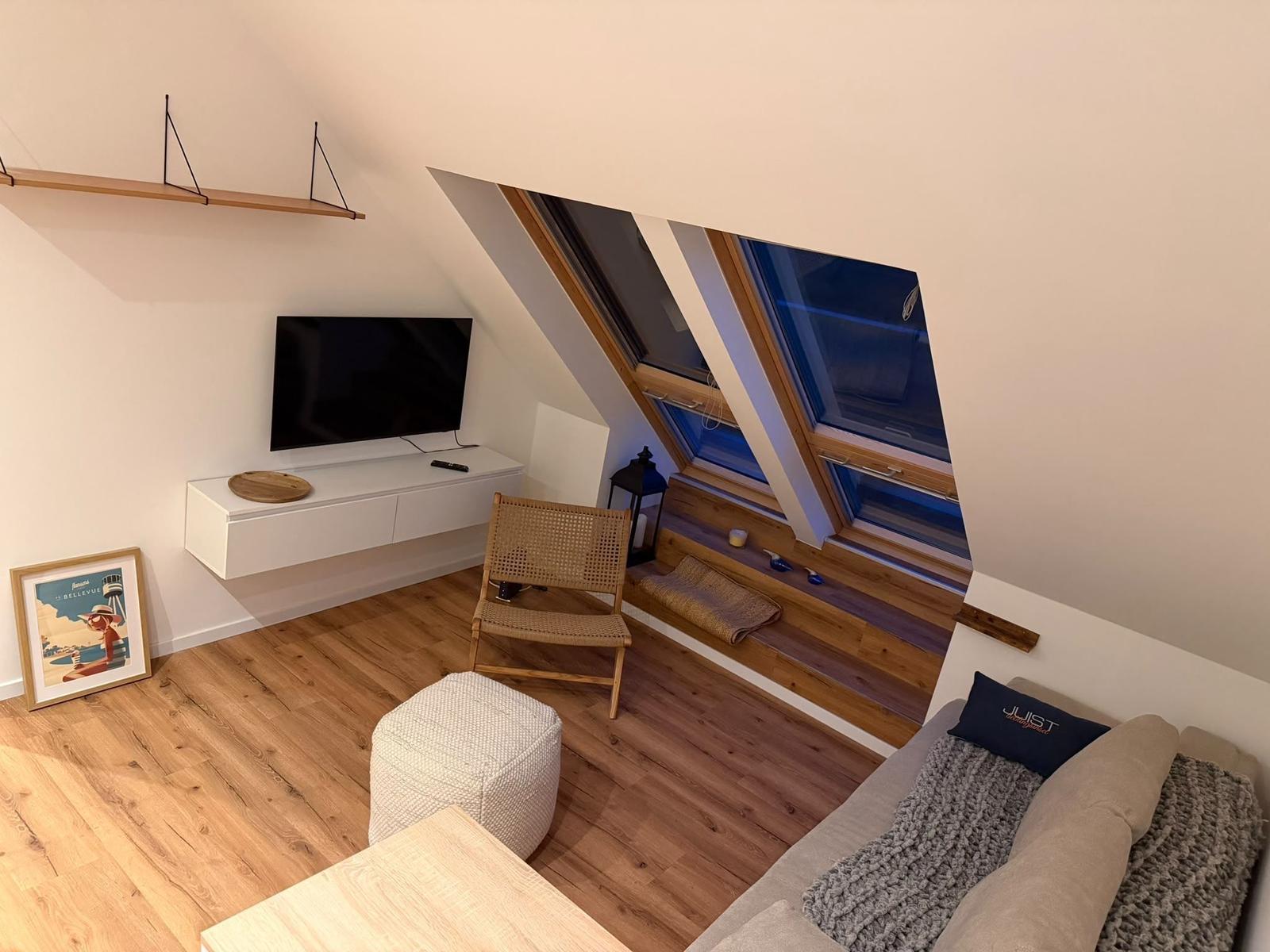 Wohnzimmer mit TV, Sitzgelegenheit und Dachfenstern.
