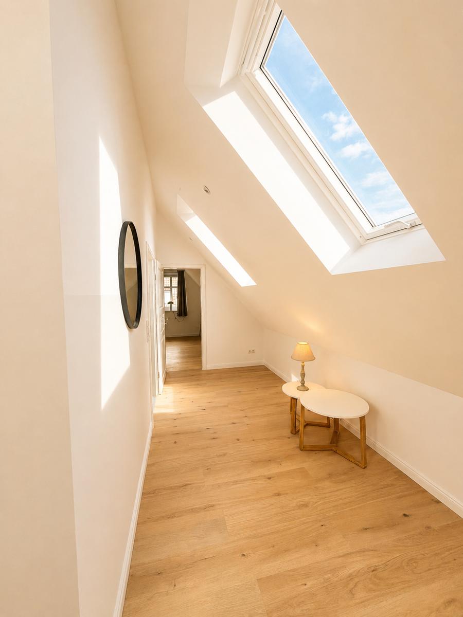 Dachgeschosszimmer mit Holzboden, Dachfenster und kleiner Tischlampe.