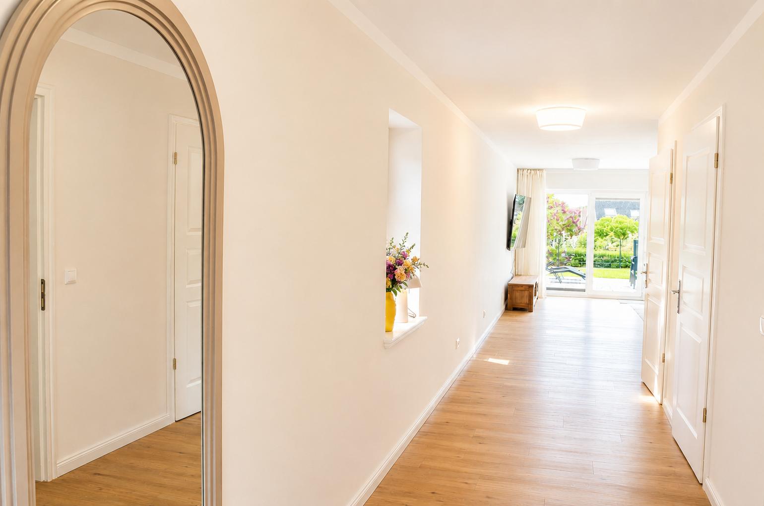 Flur mit Holzboden, weißen Wänden und Tür zu Wohnzimmer mit Gartenansicht.
