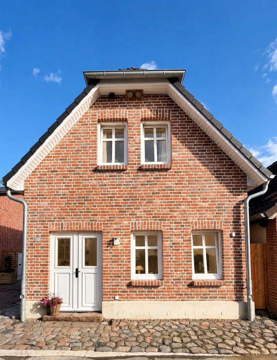 Zweistöckiges Backsteinhaus mit weißen Fenstern und Eingangstür. Kiesweg vor dem Haus.
