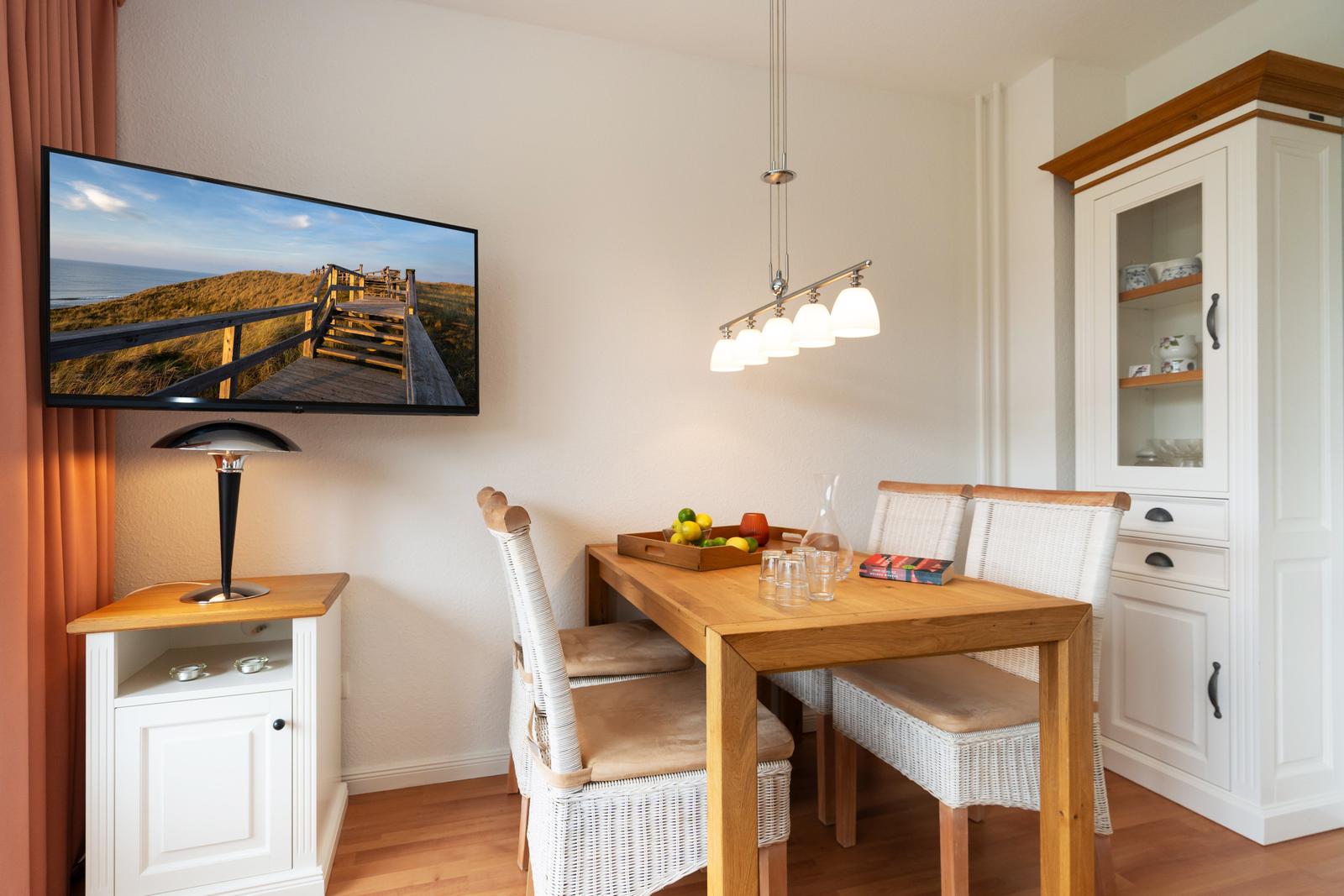 Essbereich mit Holztisch, Stühlen und TV an der Wand.