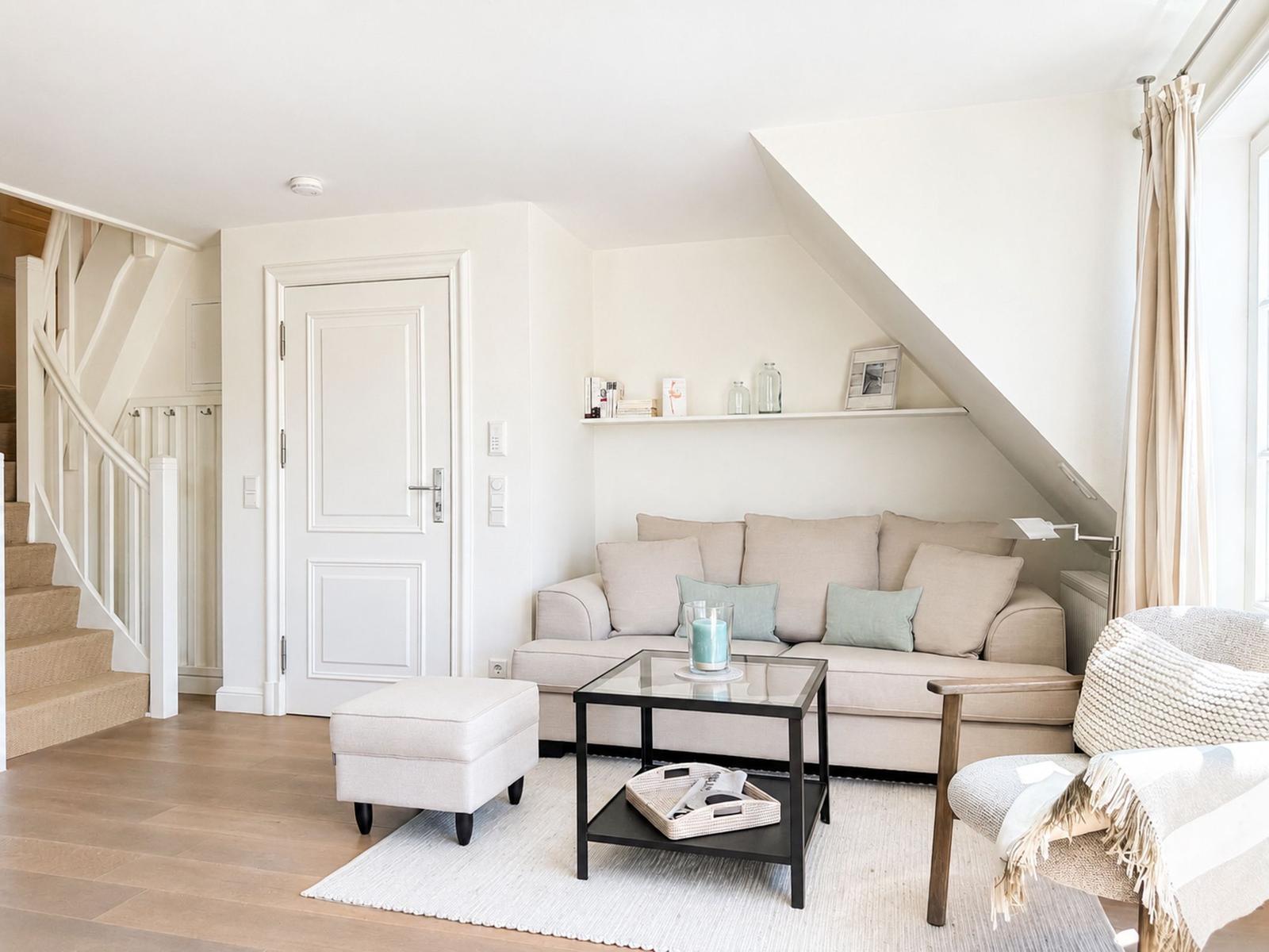 Wohnzimmer mit Sofa, Sessel und Glas-Tisch unter schräger Decke