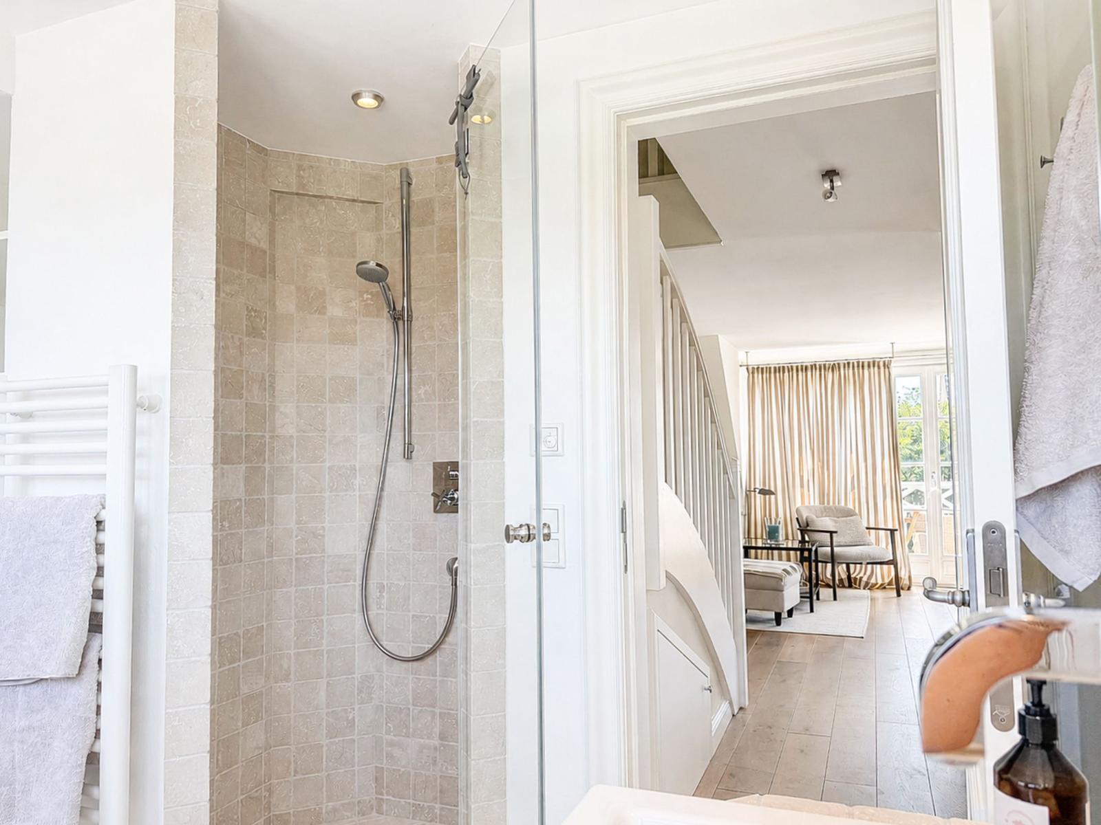 Dusche mit Glaswand, Badewanne und Blick in Wohnbereich mit Treppe.