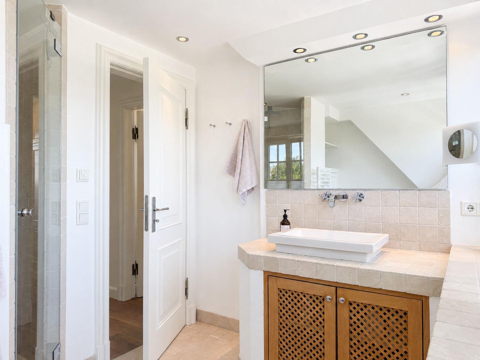 Badezimmer mit Dusche, Waschbecken und Spiegel. Holzschränke und Fliesen.