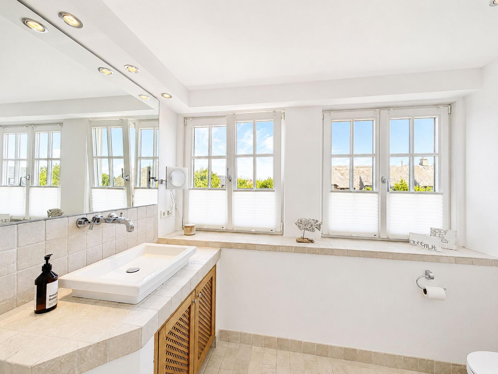 Badezimmer mit Waschbecken, Spiegel und Fenstern mit Blick auf Dächer.
