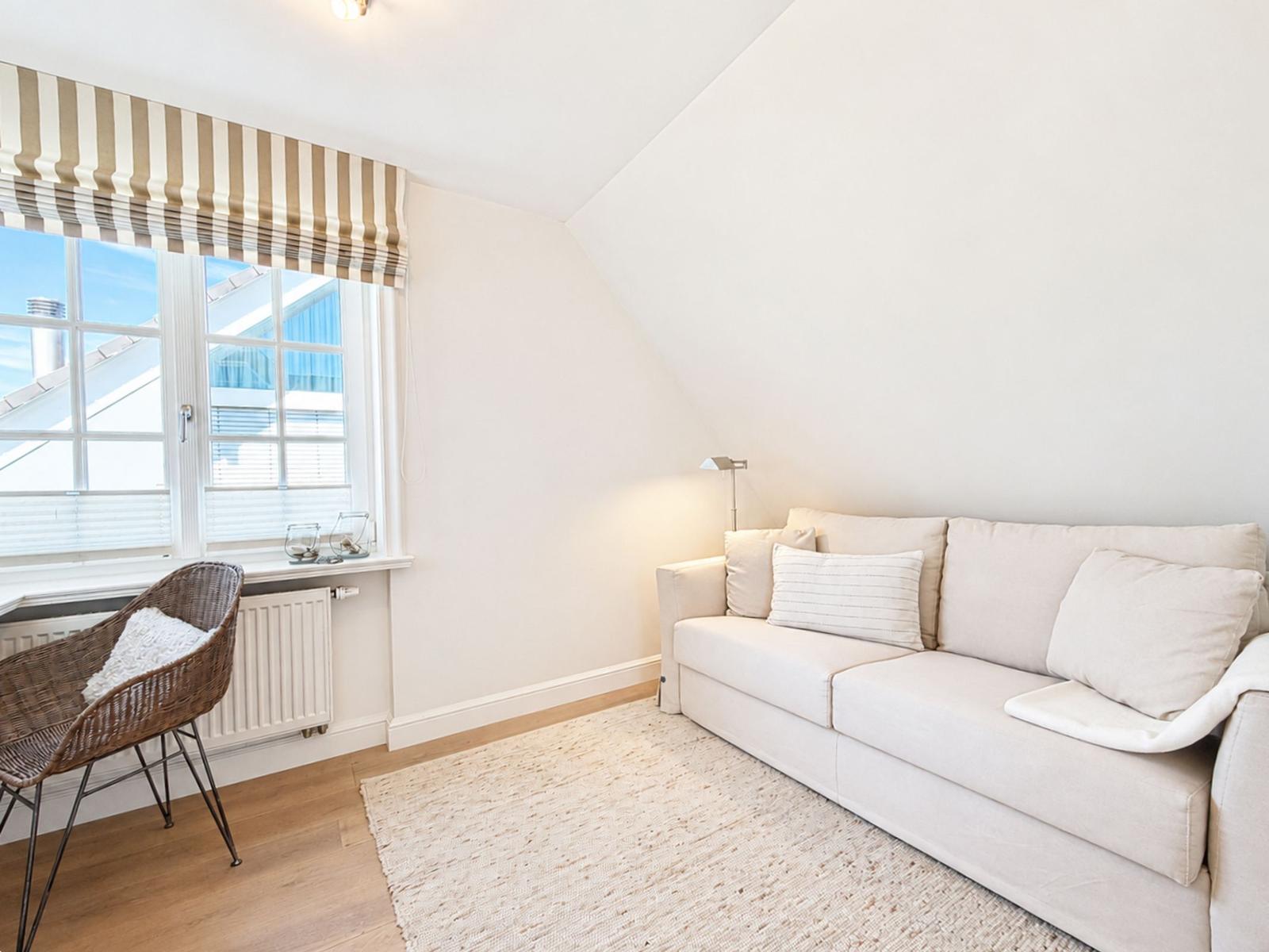 Ein Wohnzimmer mit Sofa, Sessel und Fenster mit Jalousien.