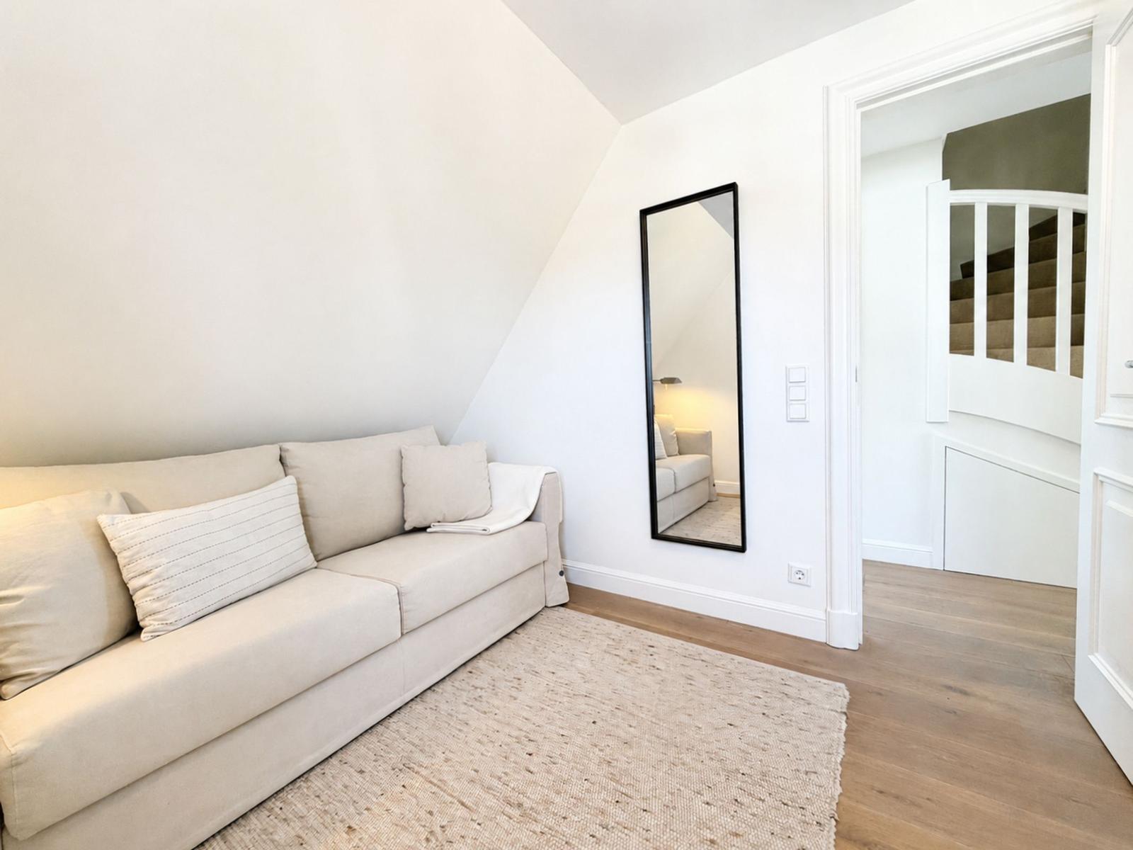 Wohnzimmer mit Sofa, Teppich und Spiegel. Treppe führt nach oben.