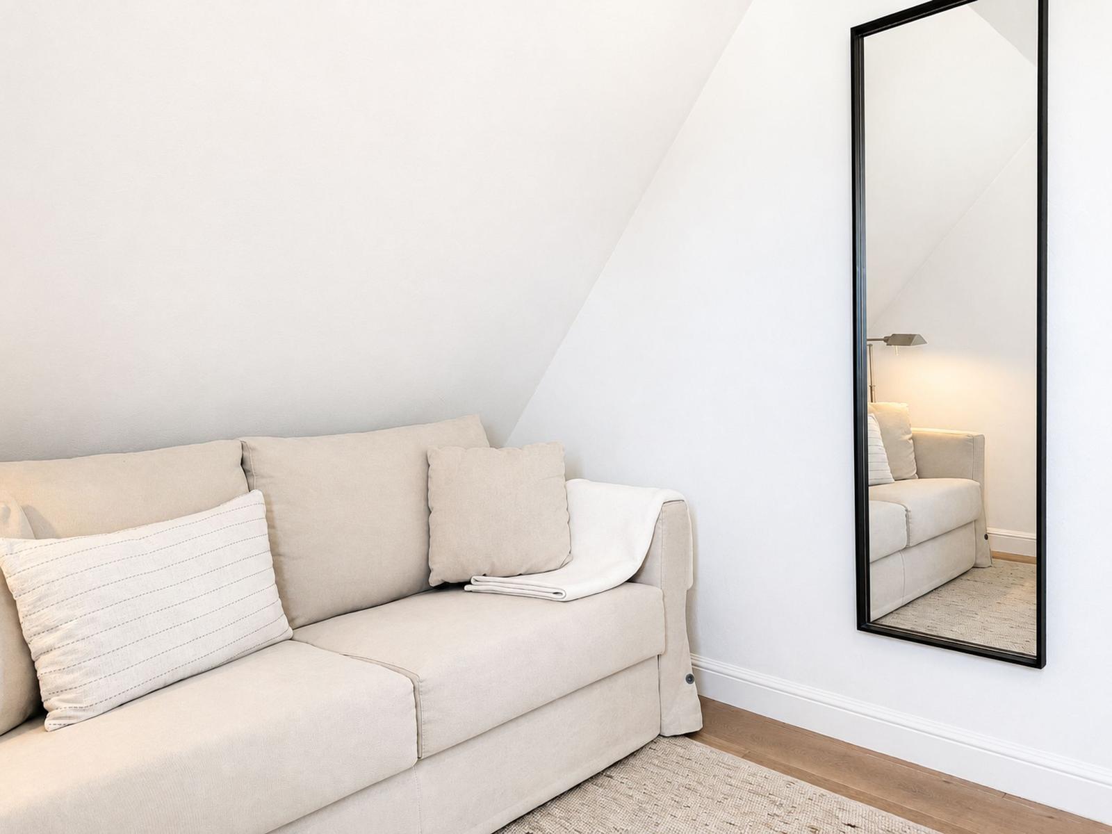 Ein Sofa mit Kissen und Decke an der Wand unter Dachschräge. Spiegel an der Wand.