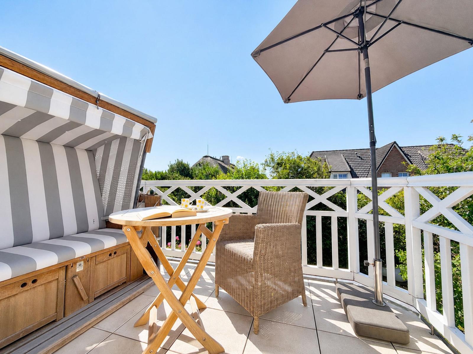 Terrasse mit Liege, Tisch und Sessel unter Sonnenschutz. Blick auf grüne Umgebung.