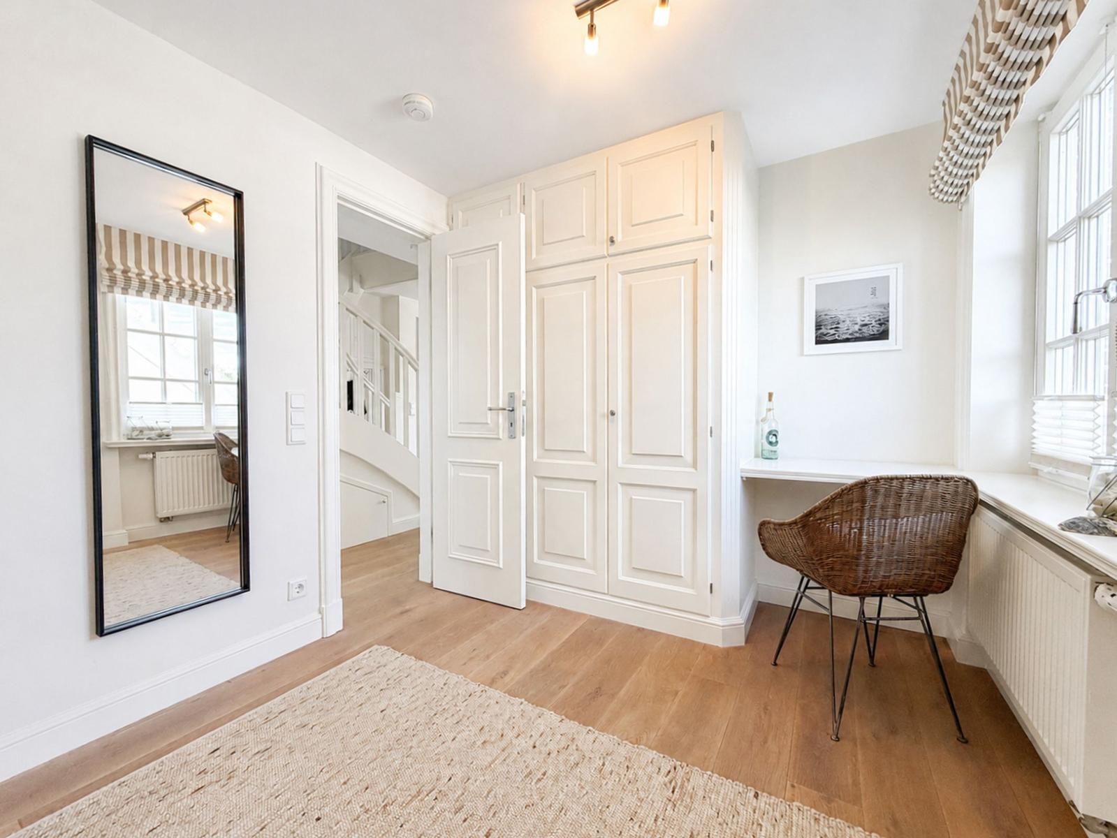 Ein Raum mit Holzboden, Spiegel, Schrank und Schreibtisch mit Stuhl.