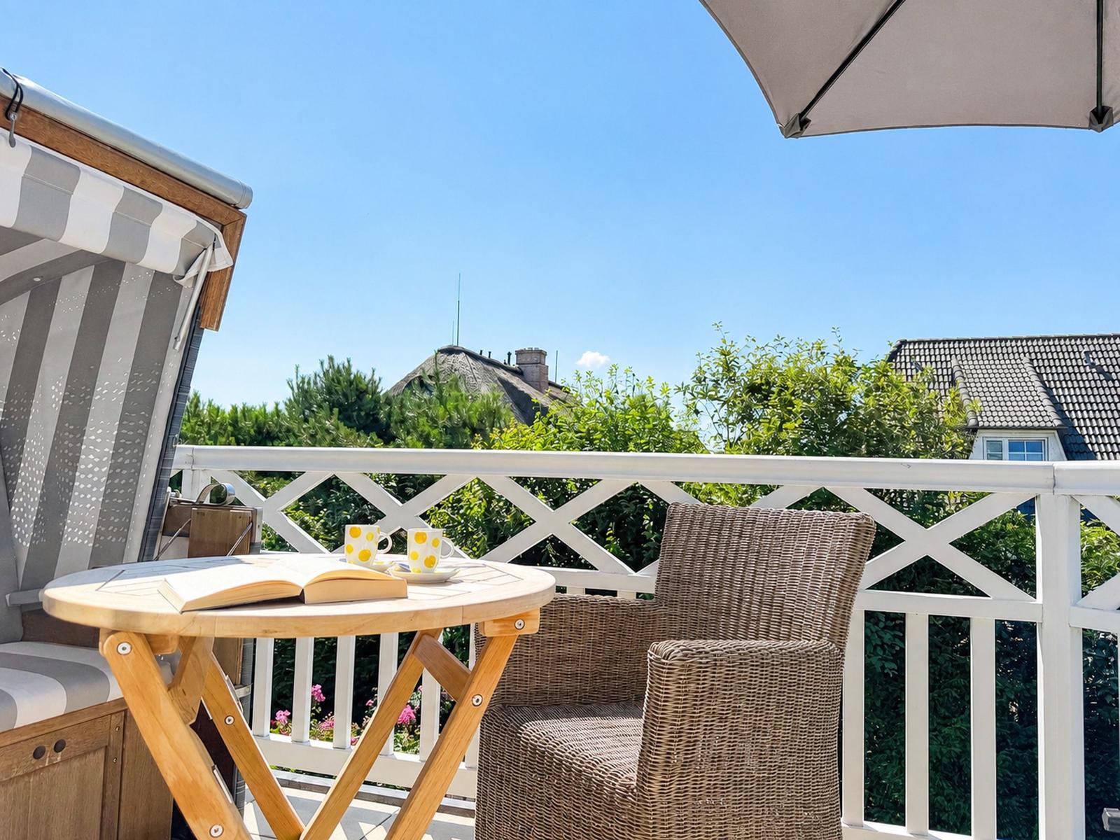 Terrasse mit Loungemöbeln, Tisch und Sonnenschutz. Blick auf Grün und Dächer.