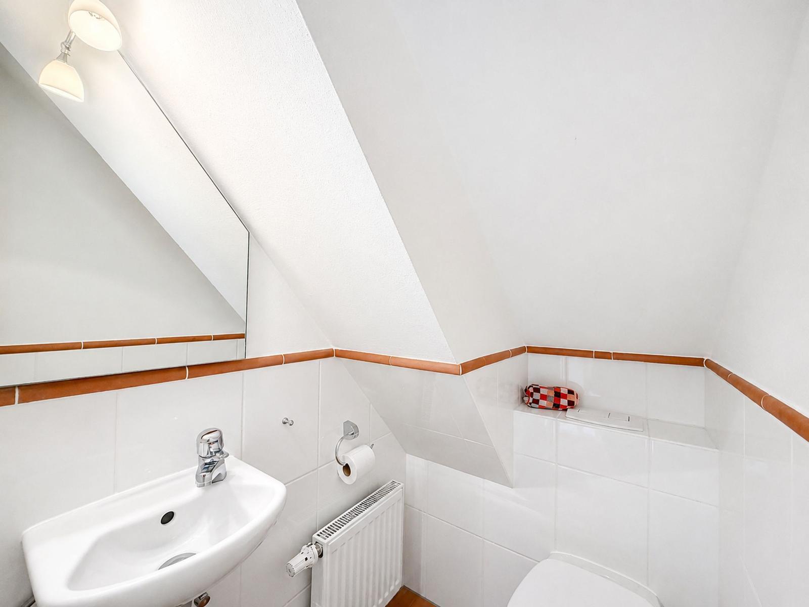 Badezimmer mit Waschbecken, Spiegel und Toilette unter schrägem Dach.