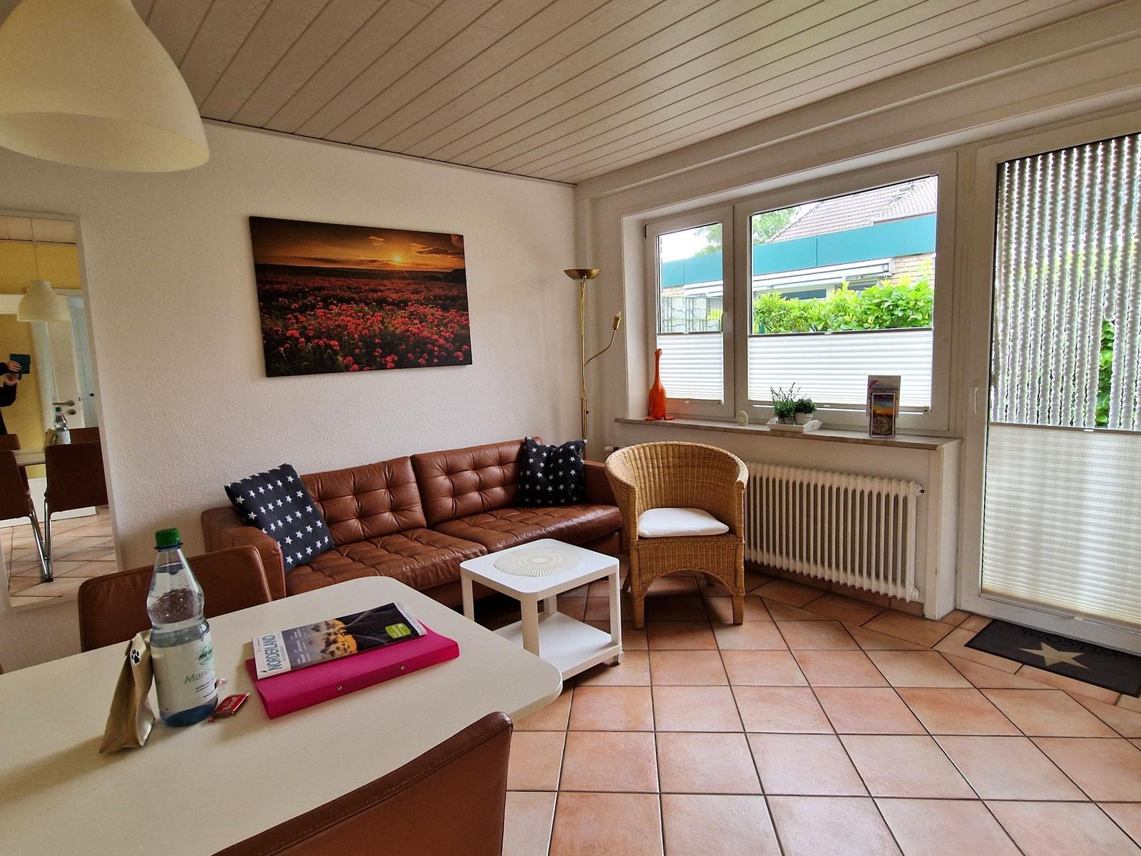 Wohnzimmer mit braunem Sofa, Wickerstuhl und Fensterblick auf Garten.