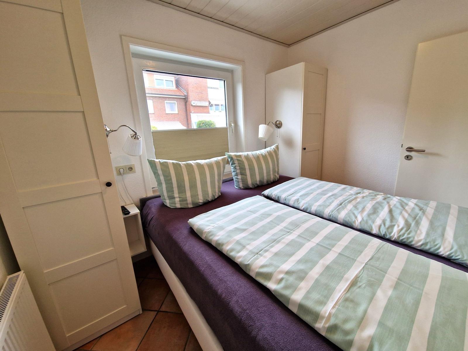 Schlafzimmer mit Doppelbett, Fenster und Nachttisch.