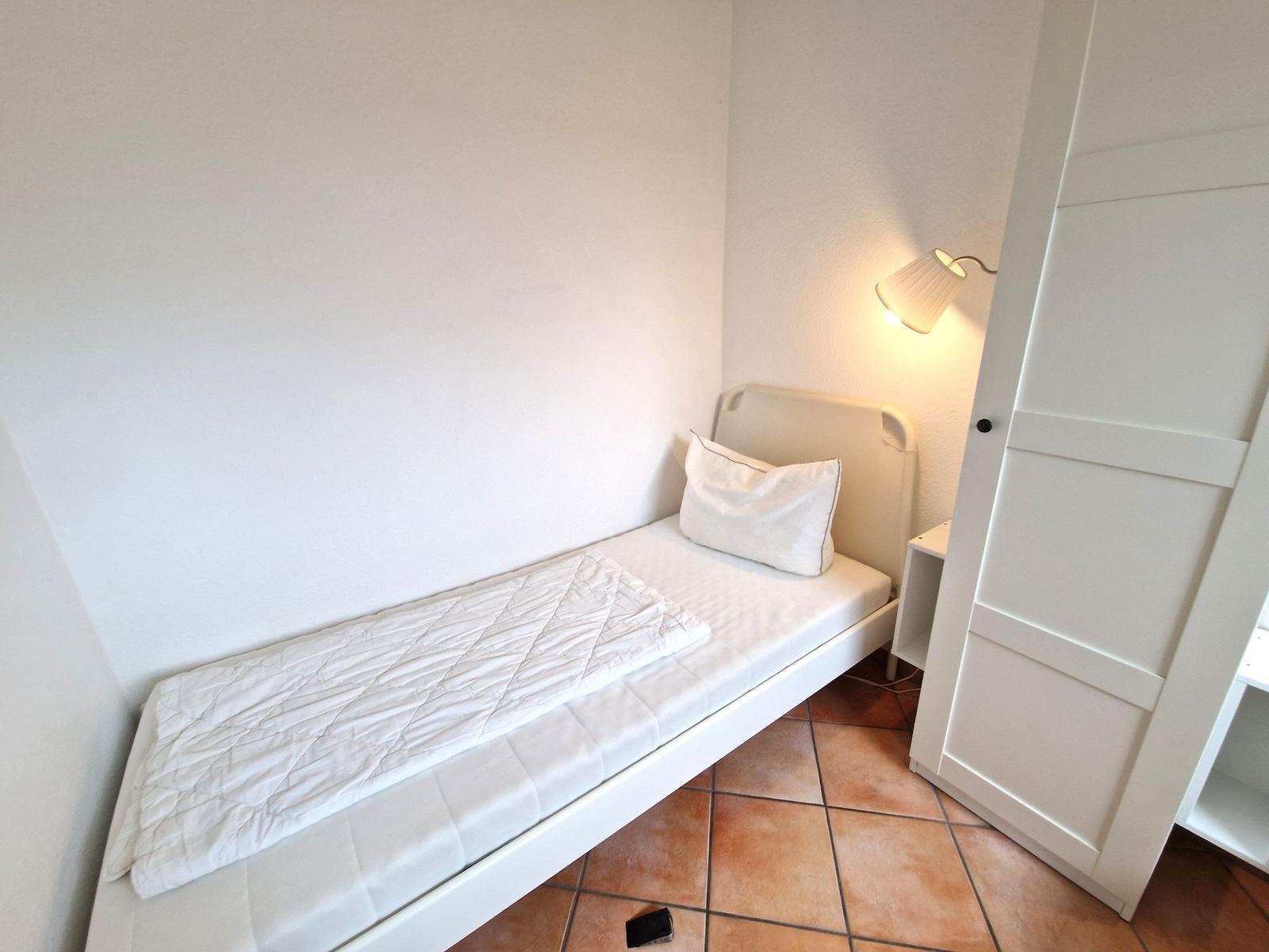 Ein Schlafzimmer mit weißem Bett, Kissen und einer Stehlampe.