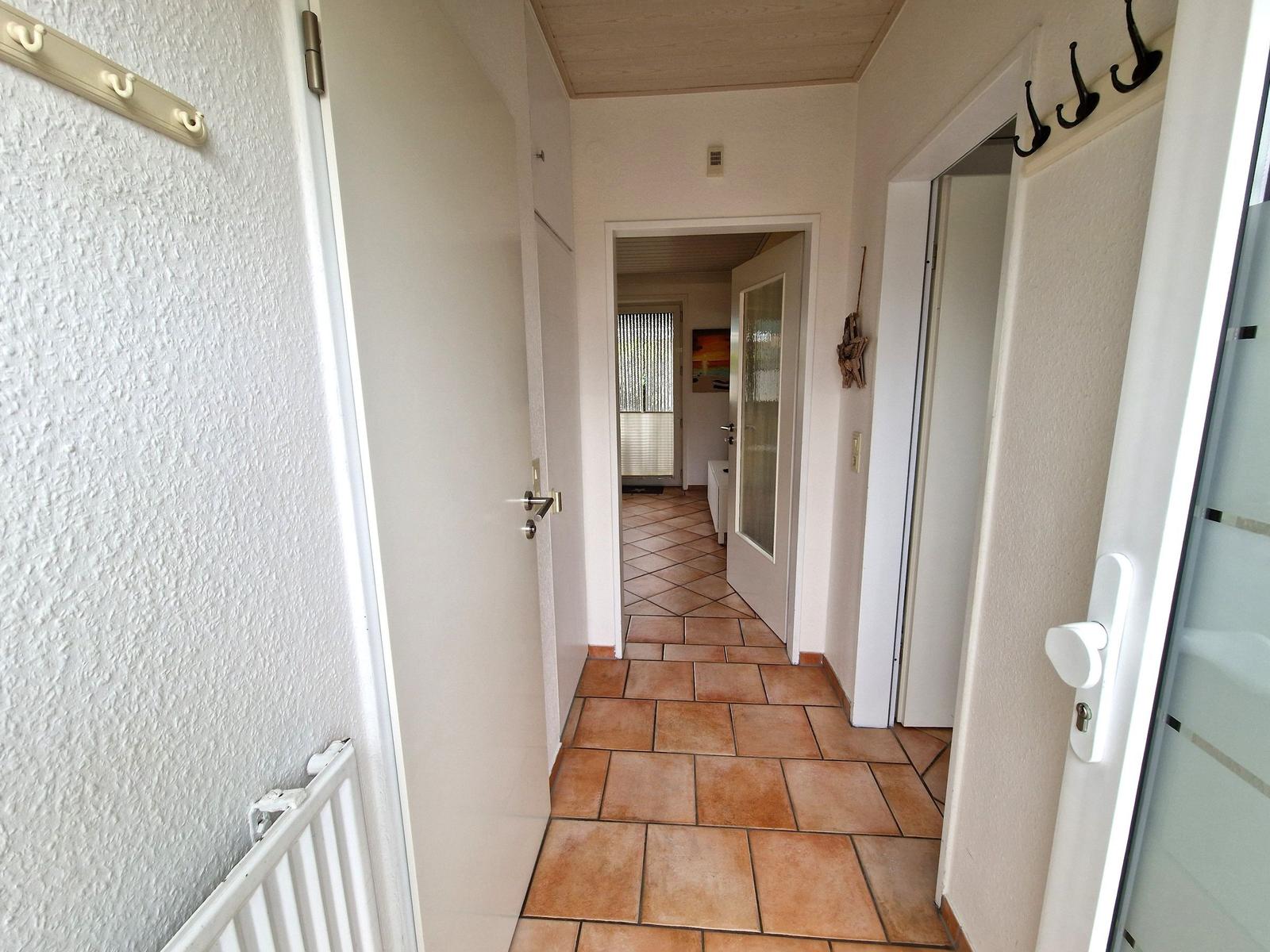Flur mit Terrakottaboden, weißen Wänden und Türen. An der Wand hängen Haken.