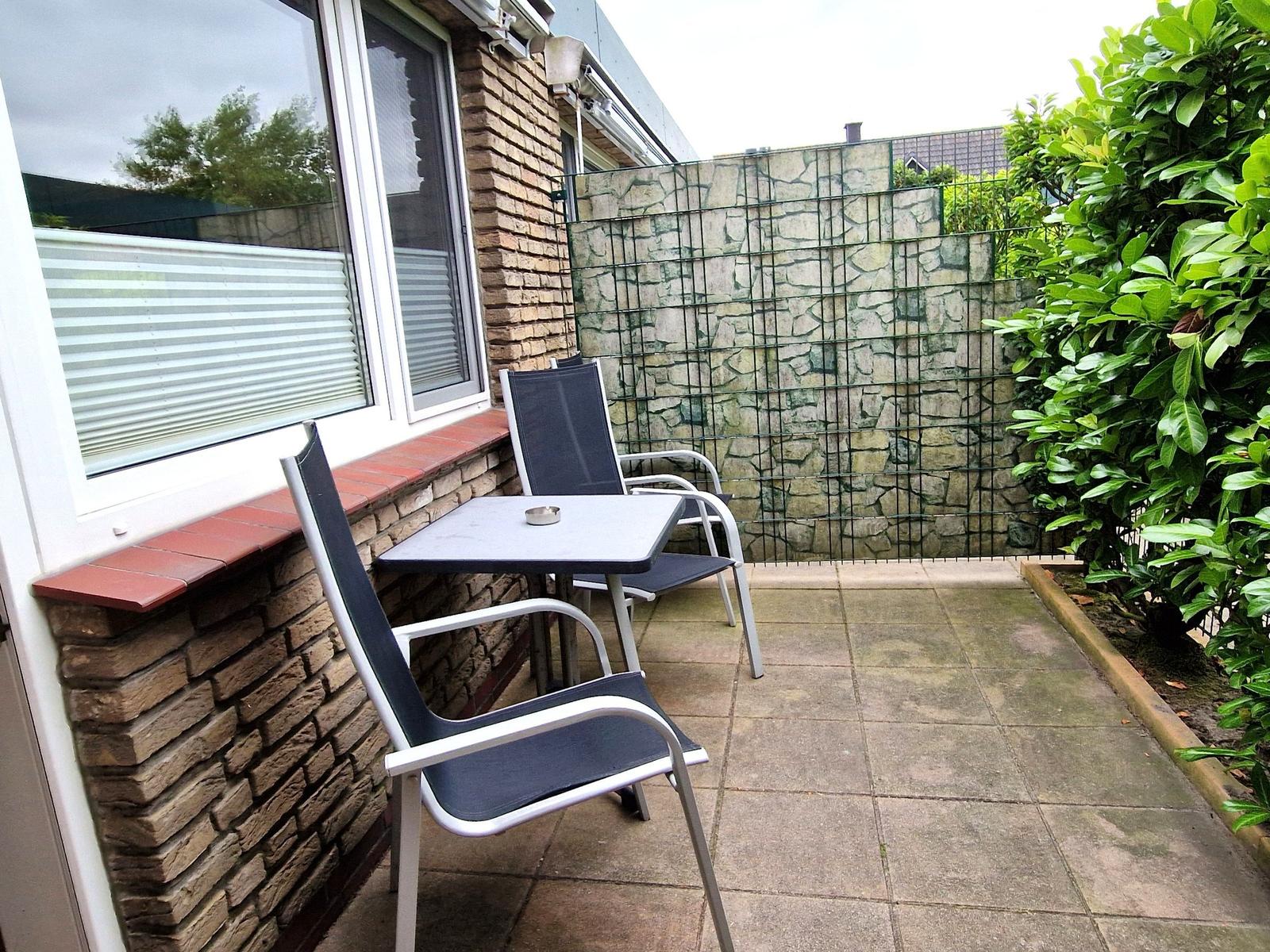 Terrasse mit Tisch und zwei Stühlen neben Fenster mit Jalousie.