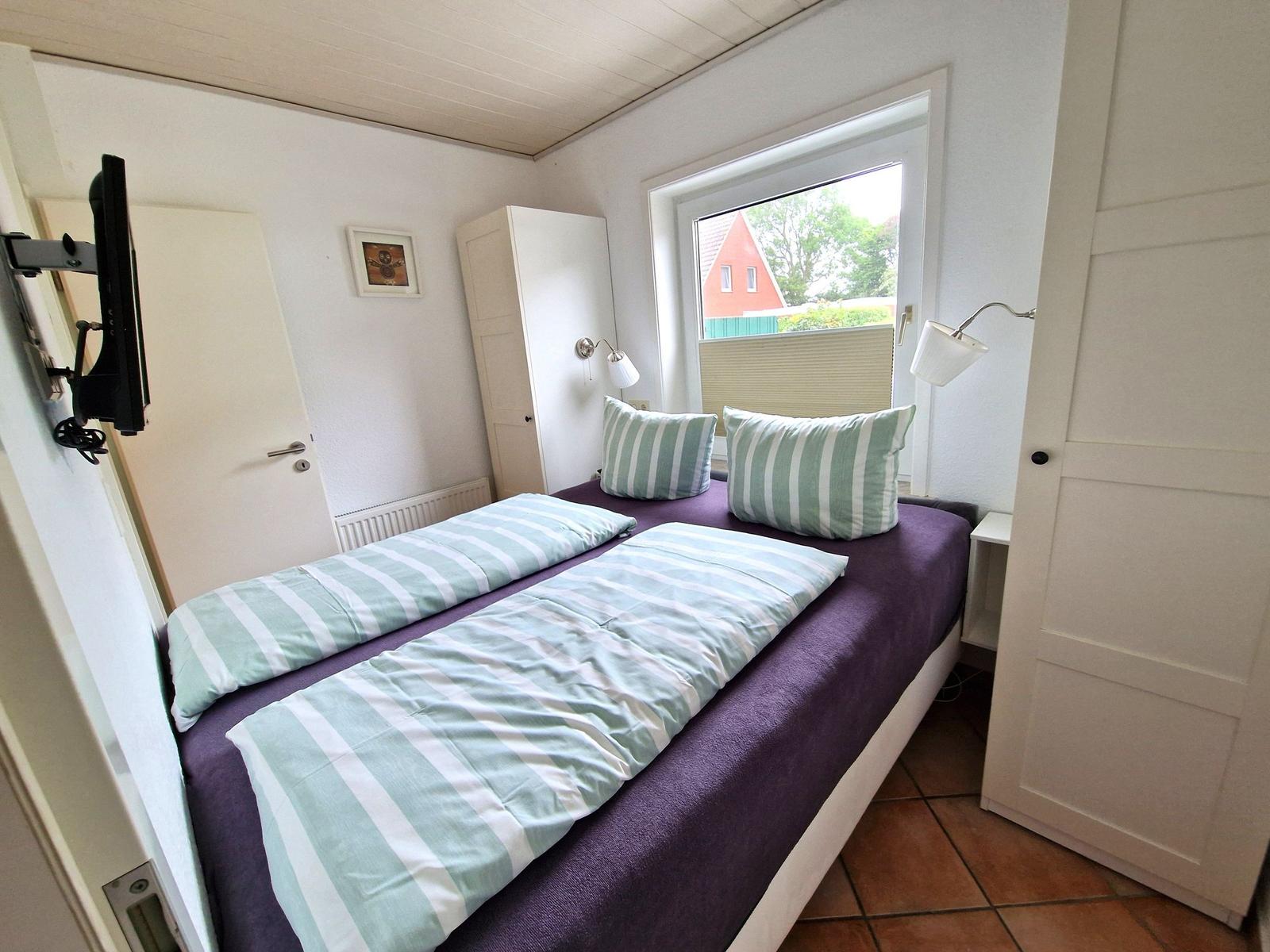 Schlafzimmer mit Doppelbett, Fenster und TV. Möbel sind weiß.